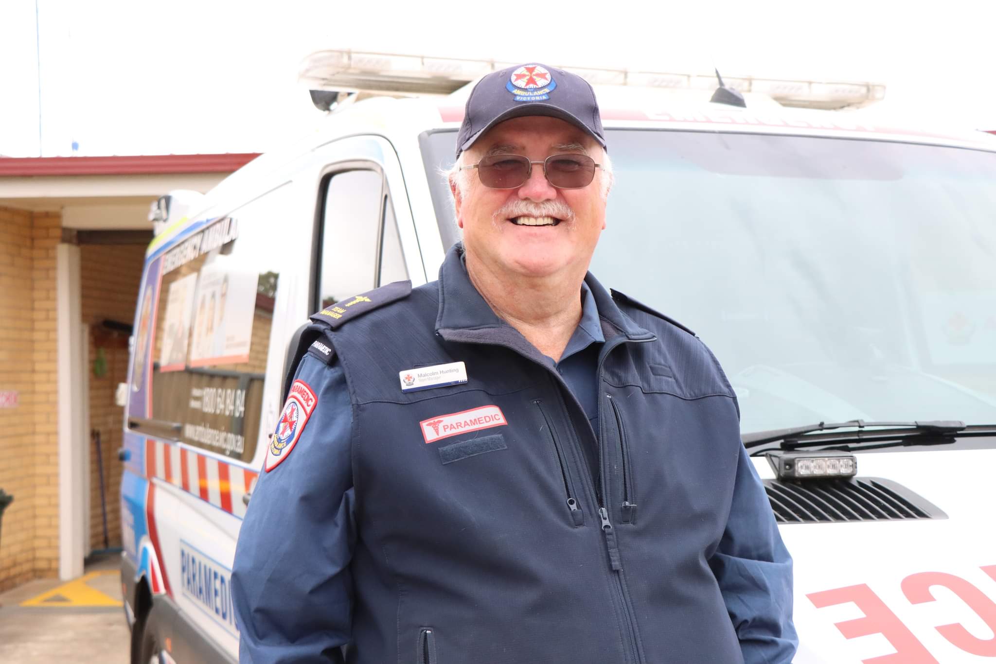 A paramedic smiles for the camera in front of an ambulance.