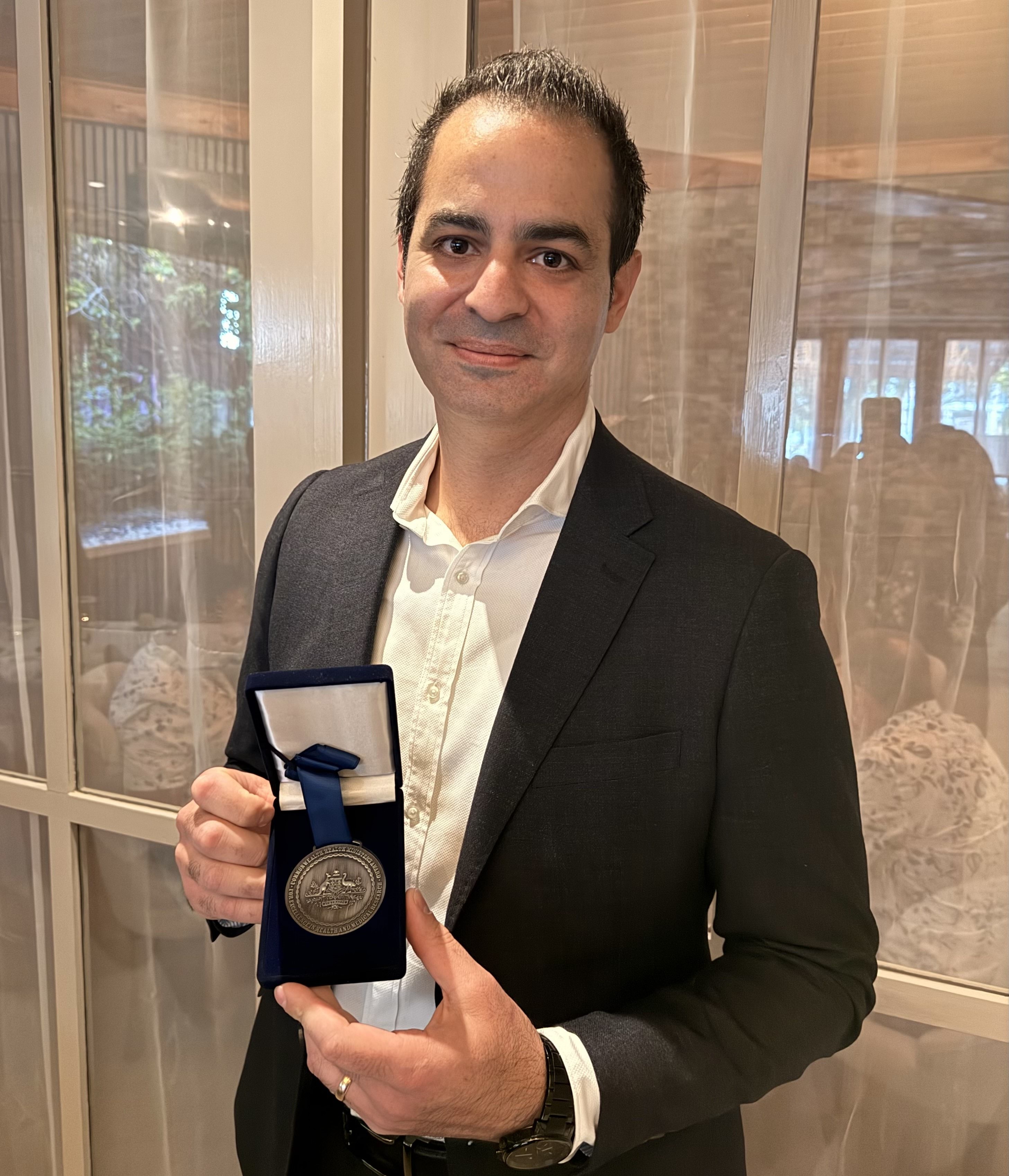A smiling man holding a medal in a box.