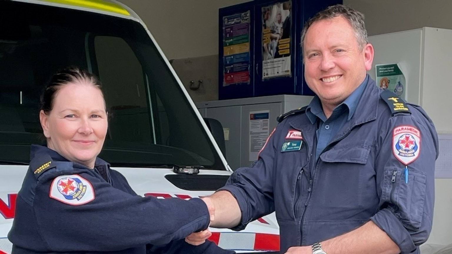 A woman and man both wearing paramedic uniforms shaking hands.