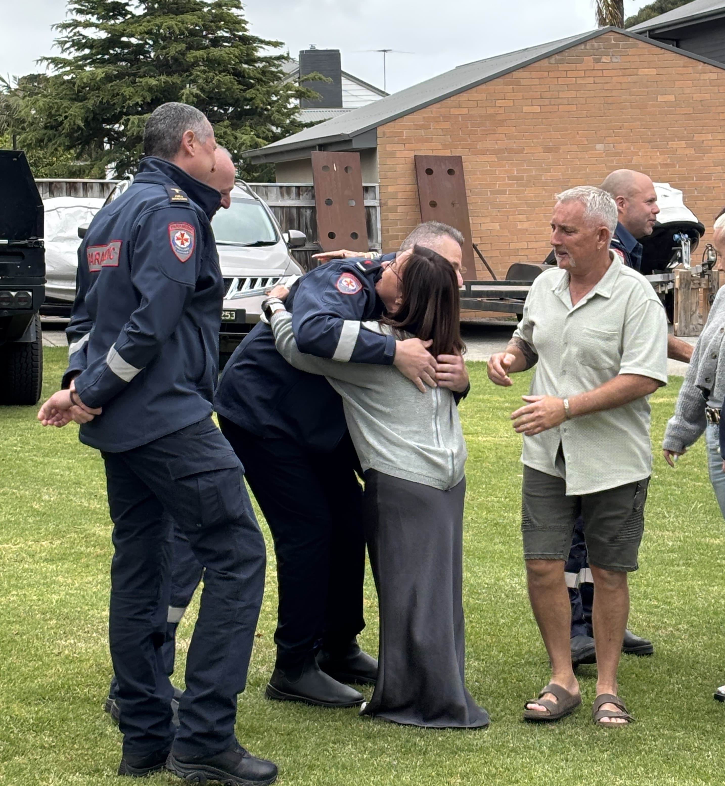 A woman hugging a paramedic surrounded by a group of people.