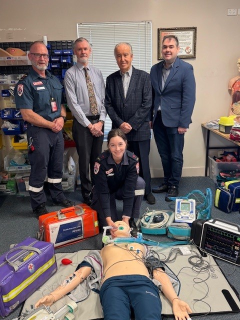 Four men and one woman standing around the new human sized training manikin.