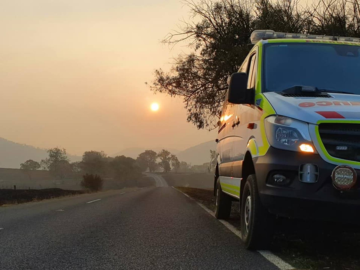 An ambulance beside a road and smokey landscape with the sun in the sky
