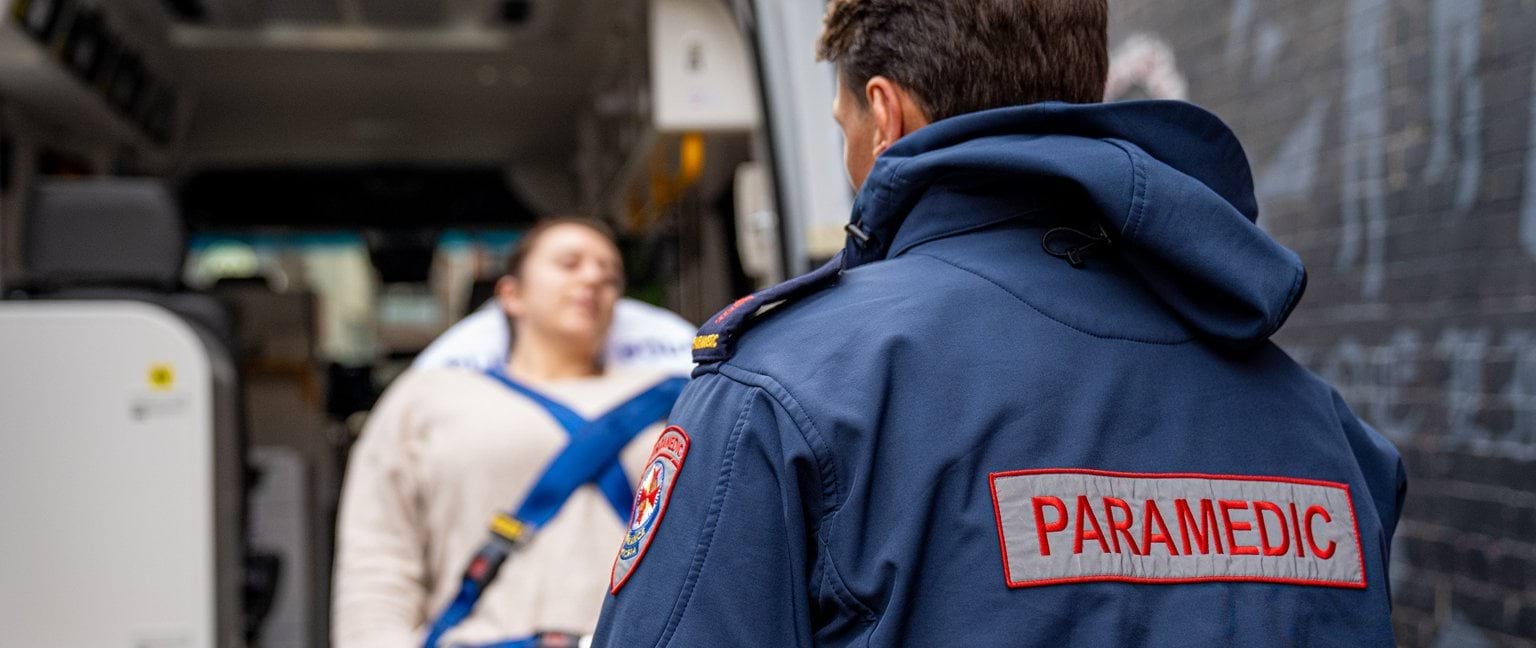 image shows a paramedic from behind as he loads a patient into an ambulance