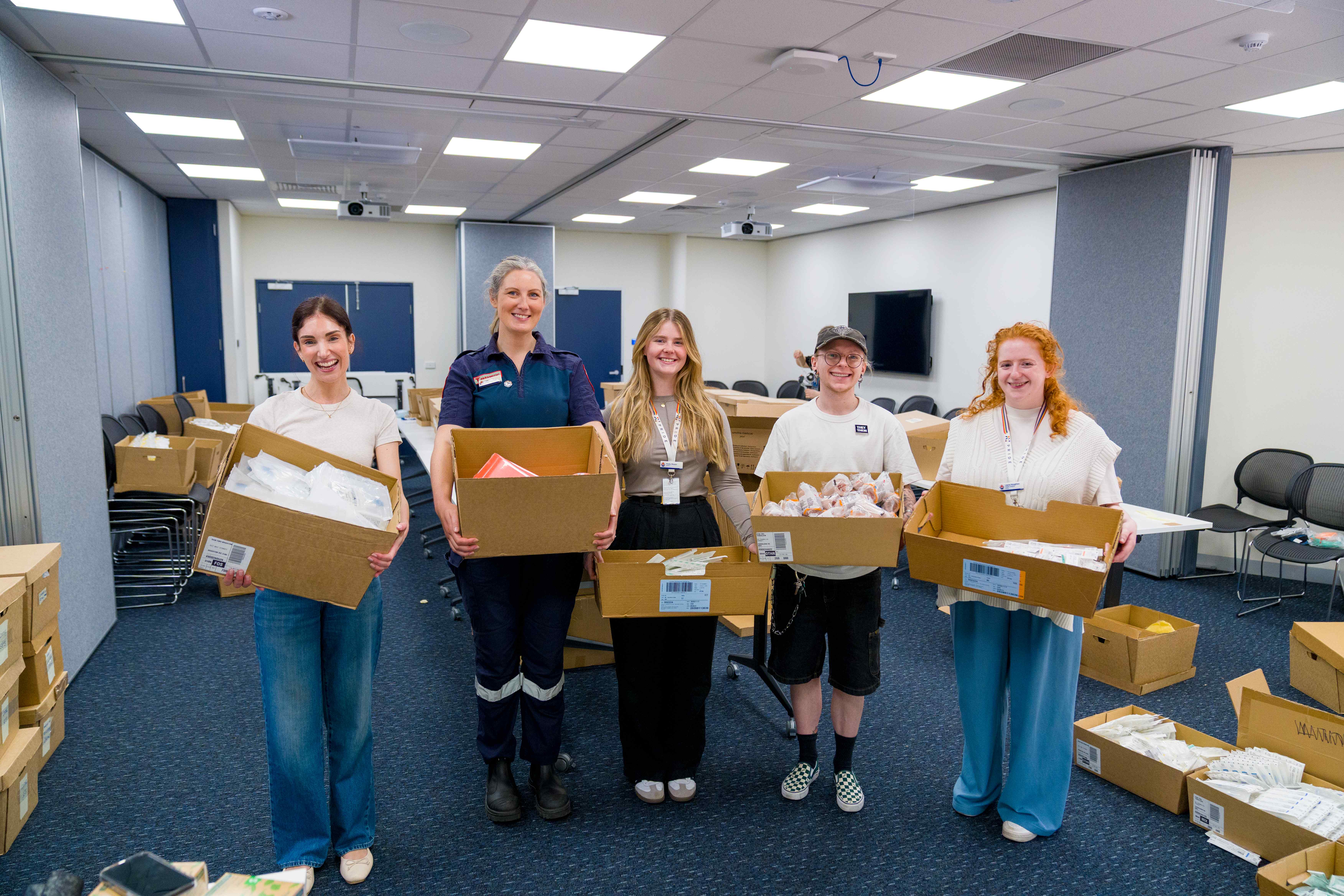 Five people smiling at the camera holding cardboard boxes filled with items.