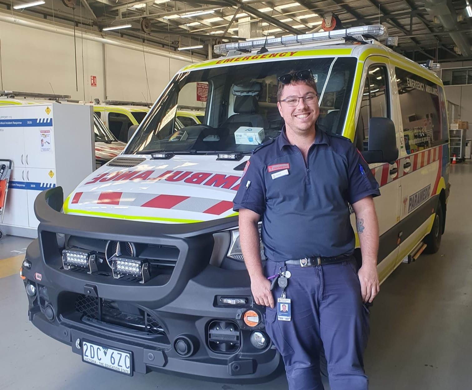 A paramedic smiles for the camera in front of an ambulance.