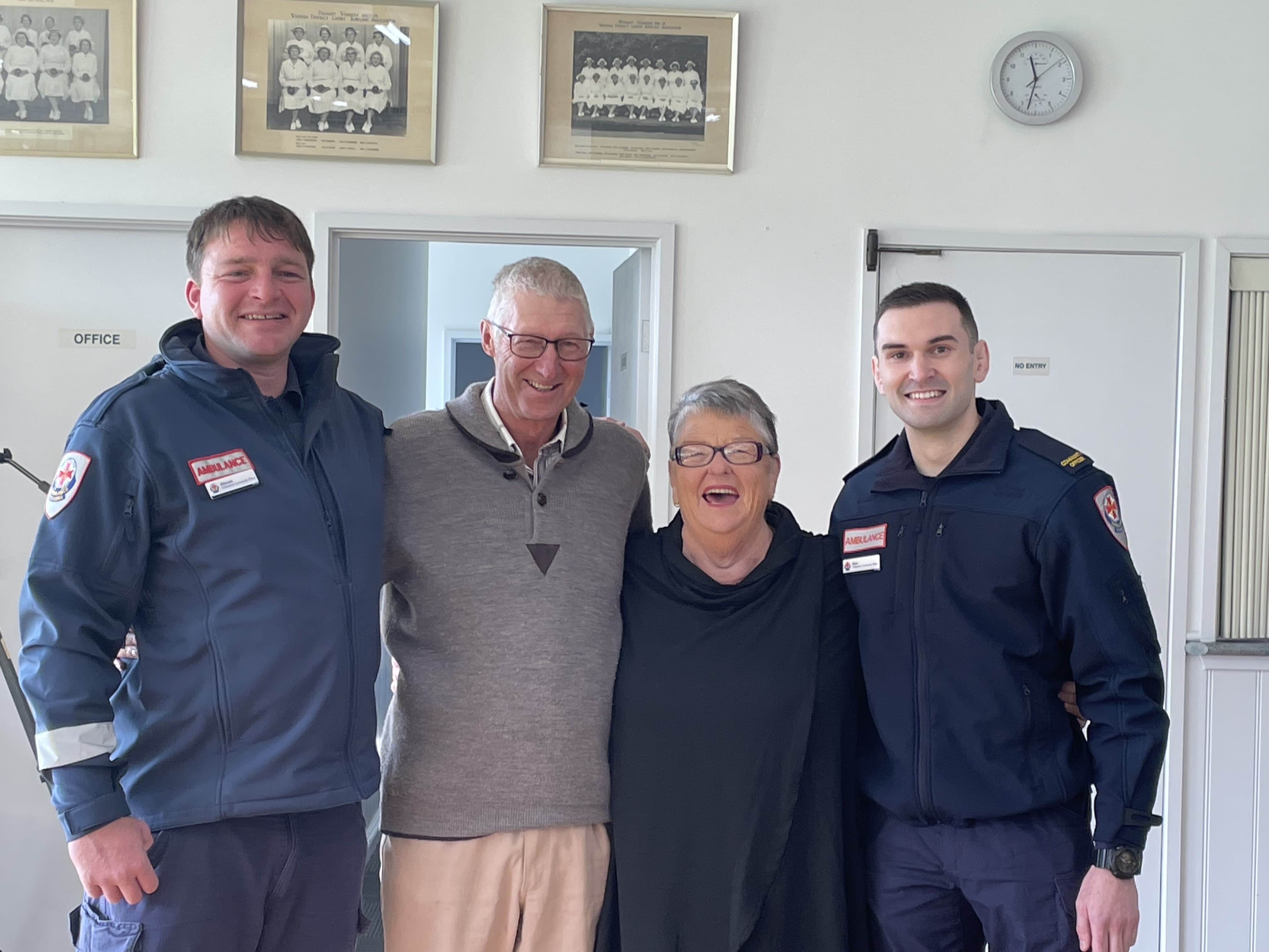 Four people smile for the camera, two in Ambulance Victoria uniform.