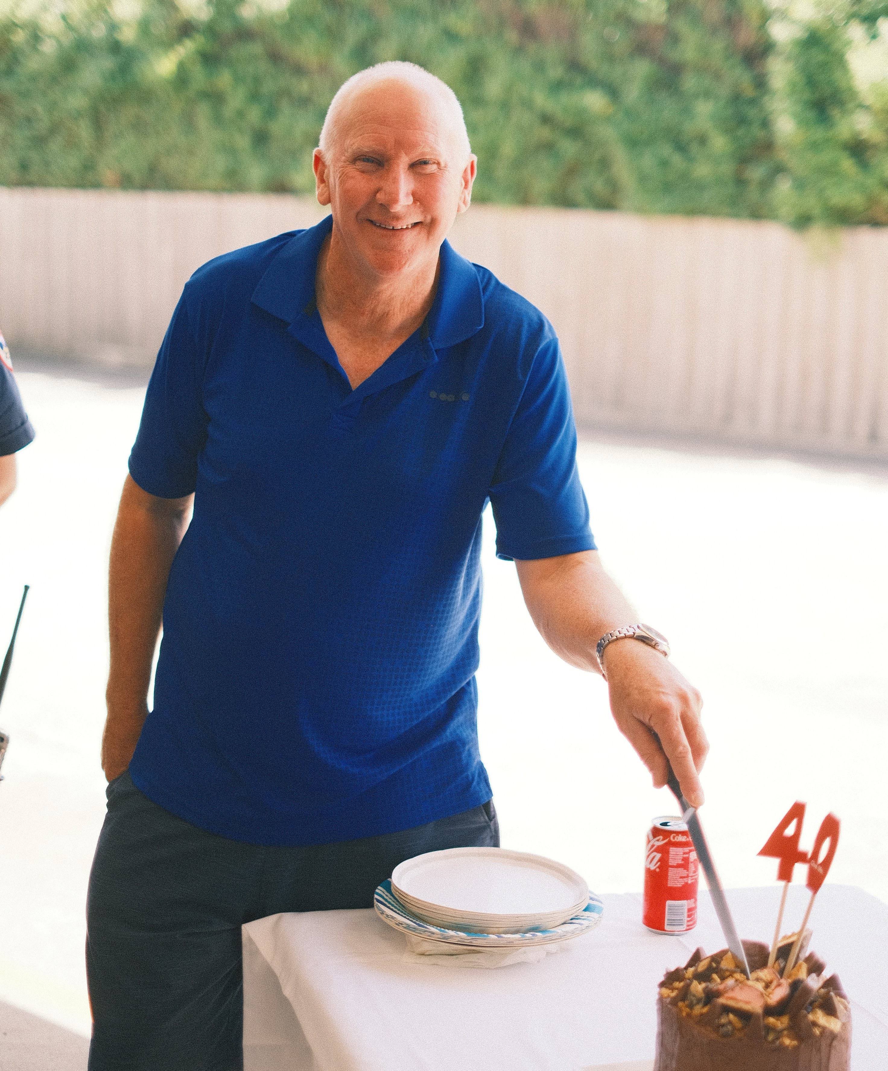 A man smiles for the camera as he cuts a cake with 40 on it.