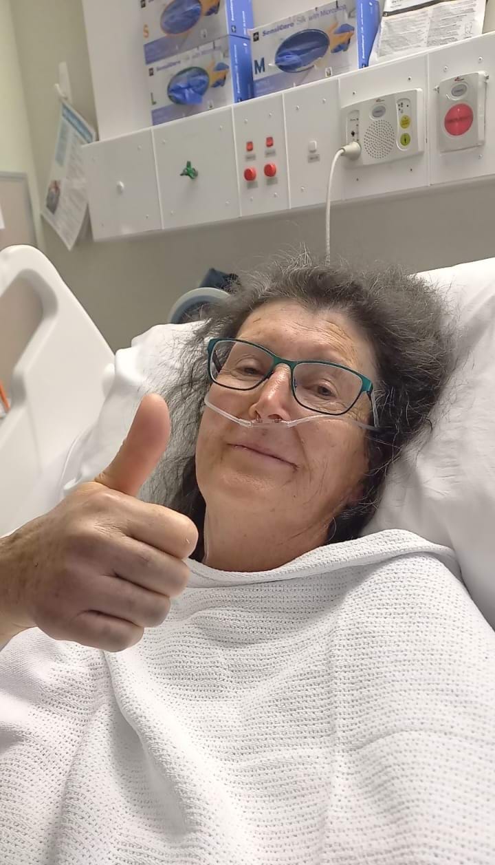 A woman laying in a hospital bed giving a thumbs up.