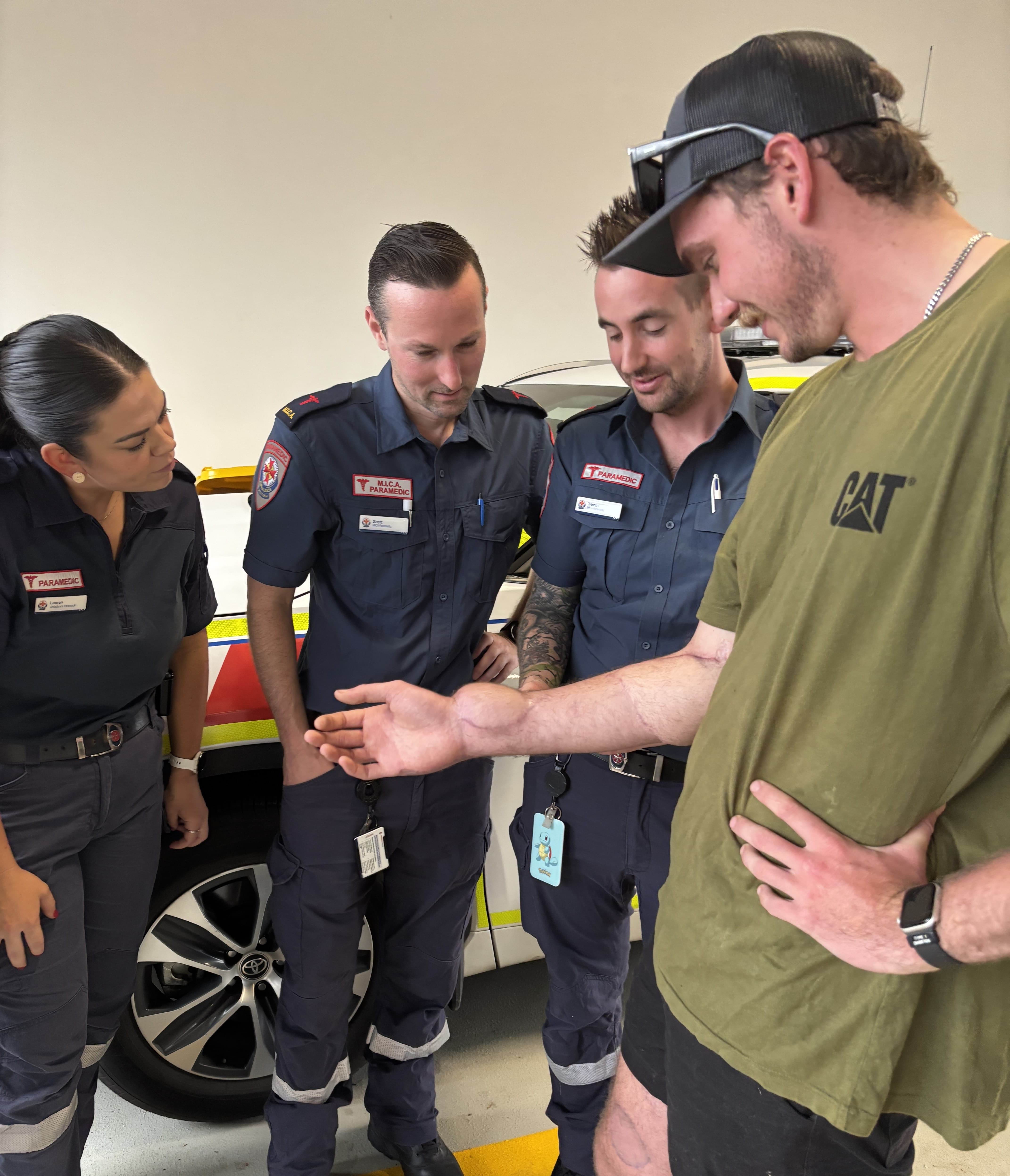 Three paramedics looking at scars on a man's right arm.