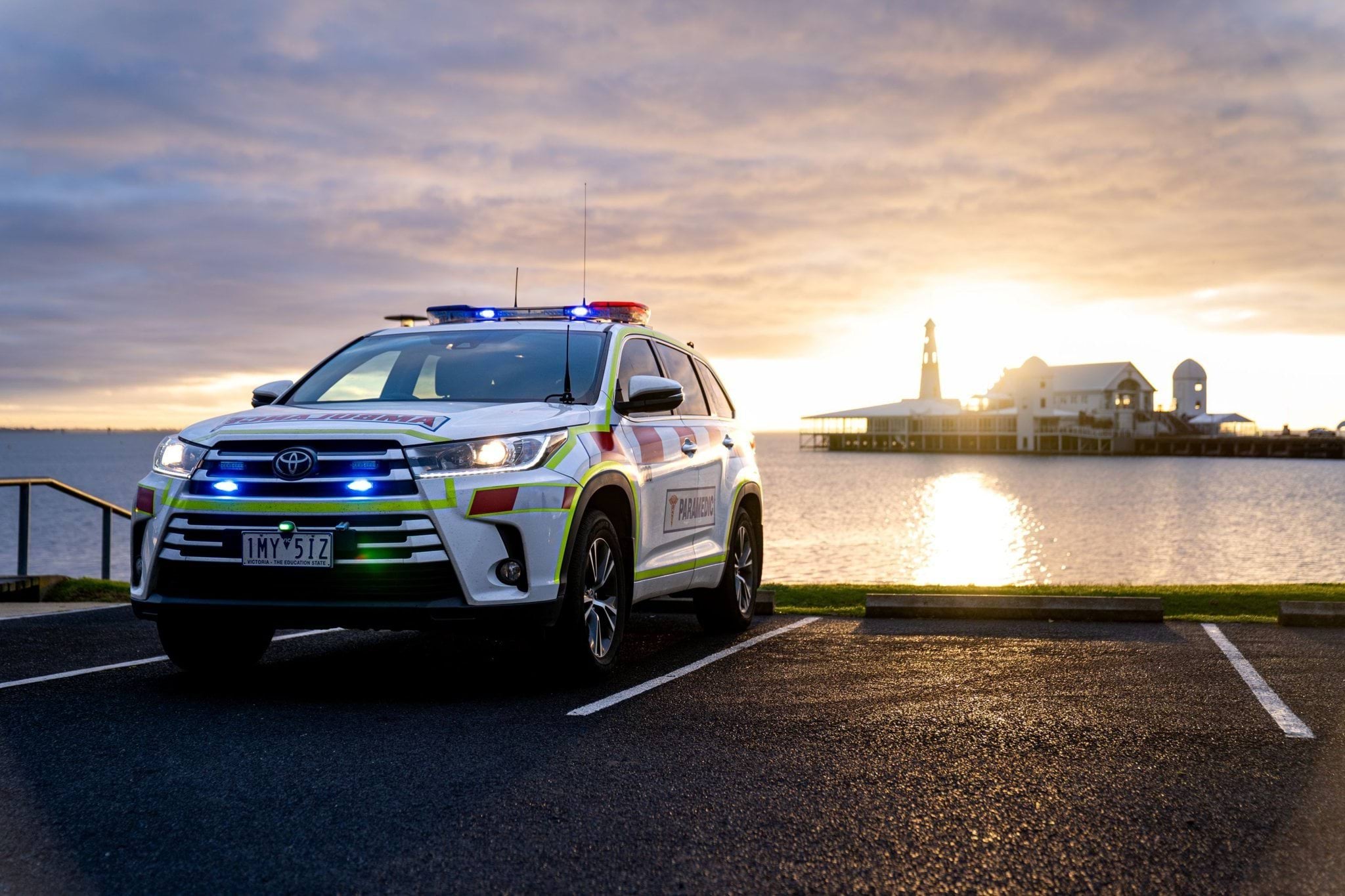 Image shows an ambulance victoria vehicle photographed in front of a scenic sunset