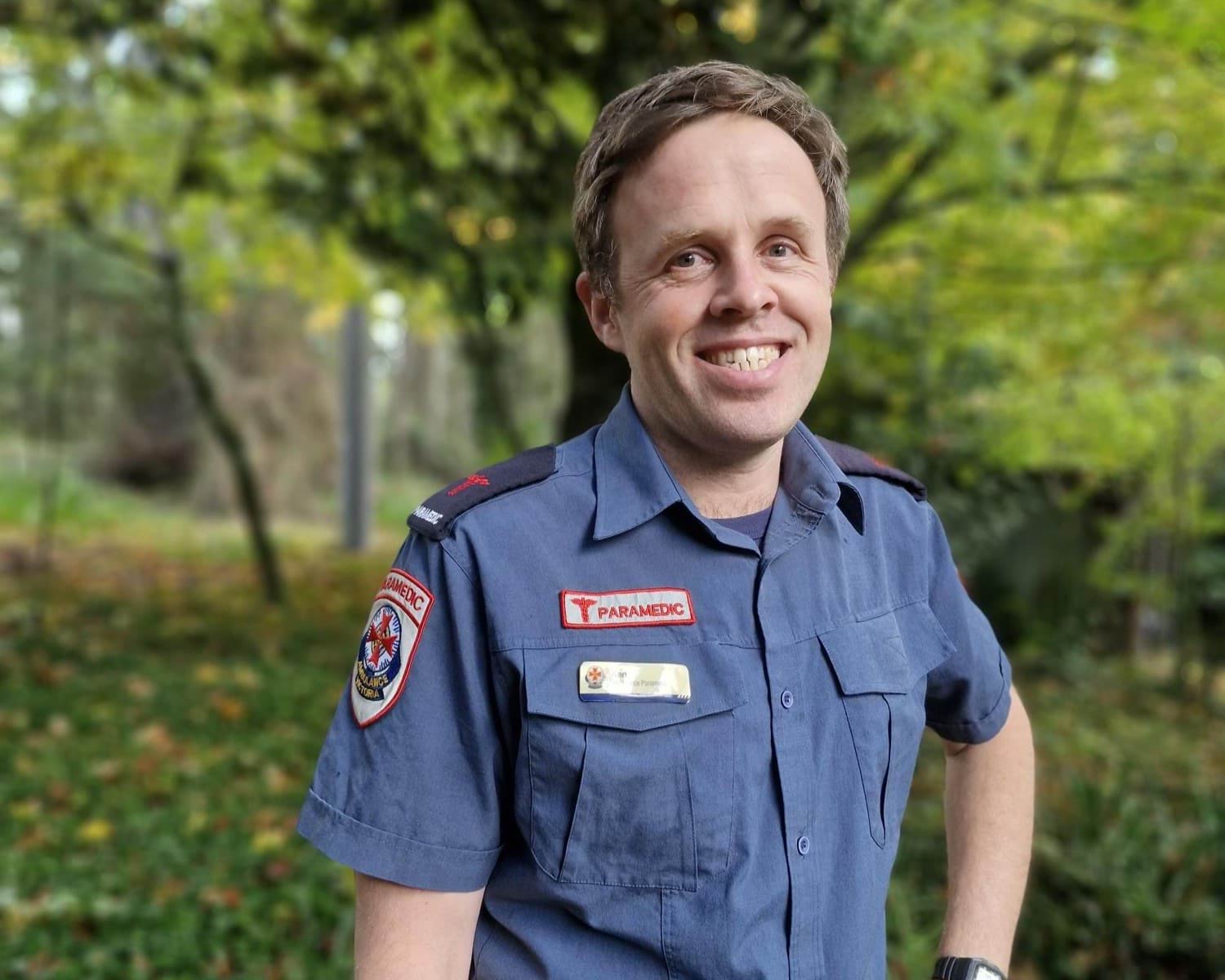An Ambulance Victoria paramedic smiles. He is outside in a garden.