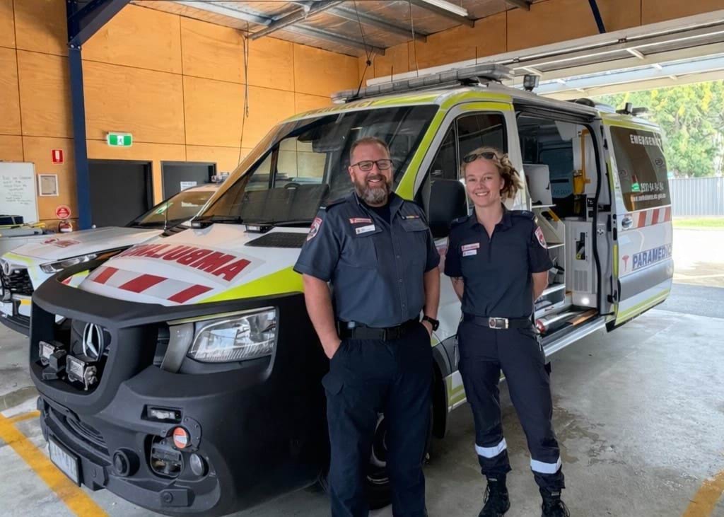 A man and woman paramedic stand in front of an ambulance vehicle.