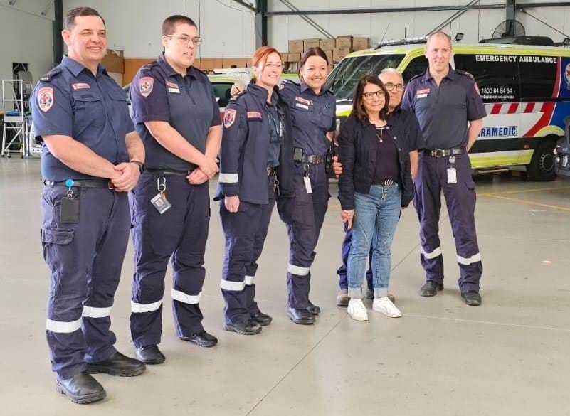 A group of paramedics stand in an Ambulance Victoria branch with a woman.