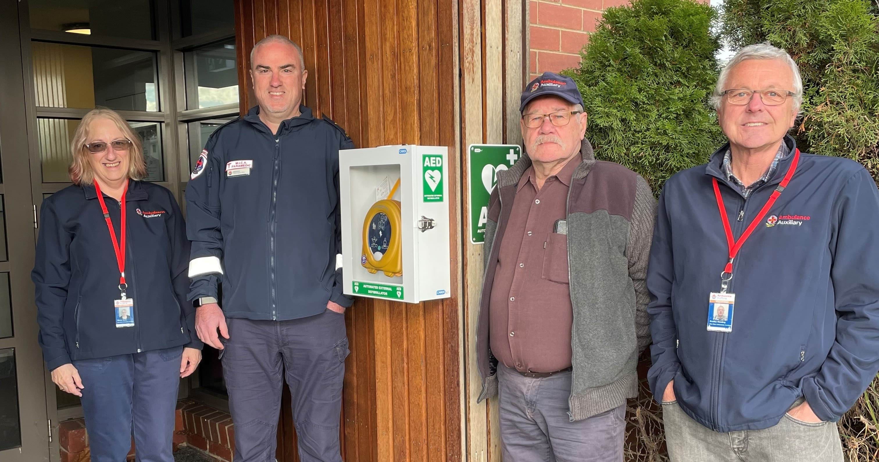 Three males and one female of the Baw Baw auxiliary team standing beside a new installed automated external defibrillators at the Warragul Ambulance Branch.