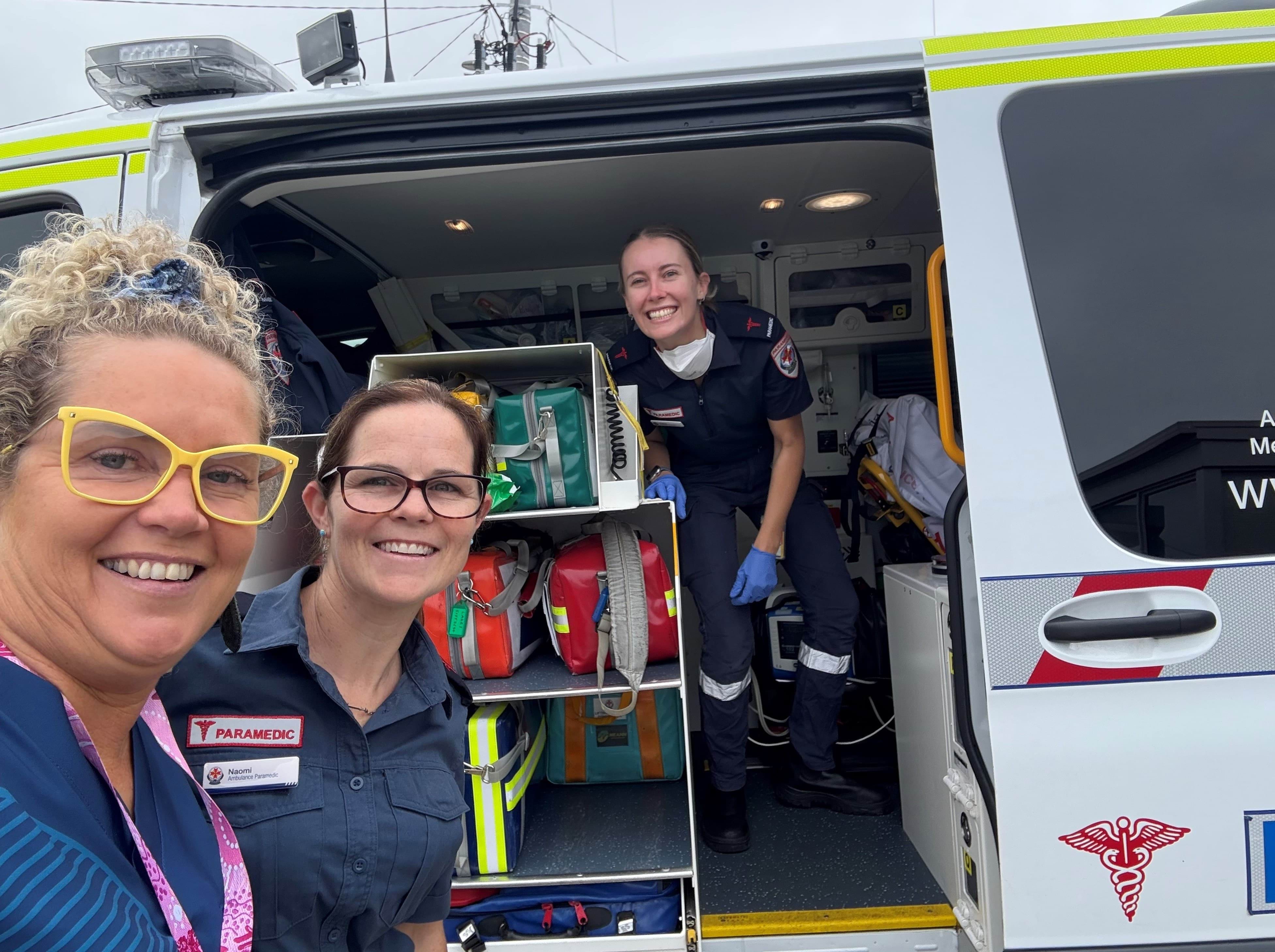 A selfie of a woman with two paramedics in the side of an ambulance.