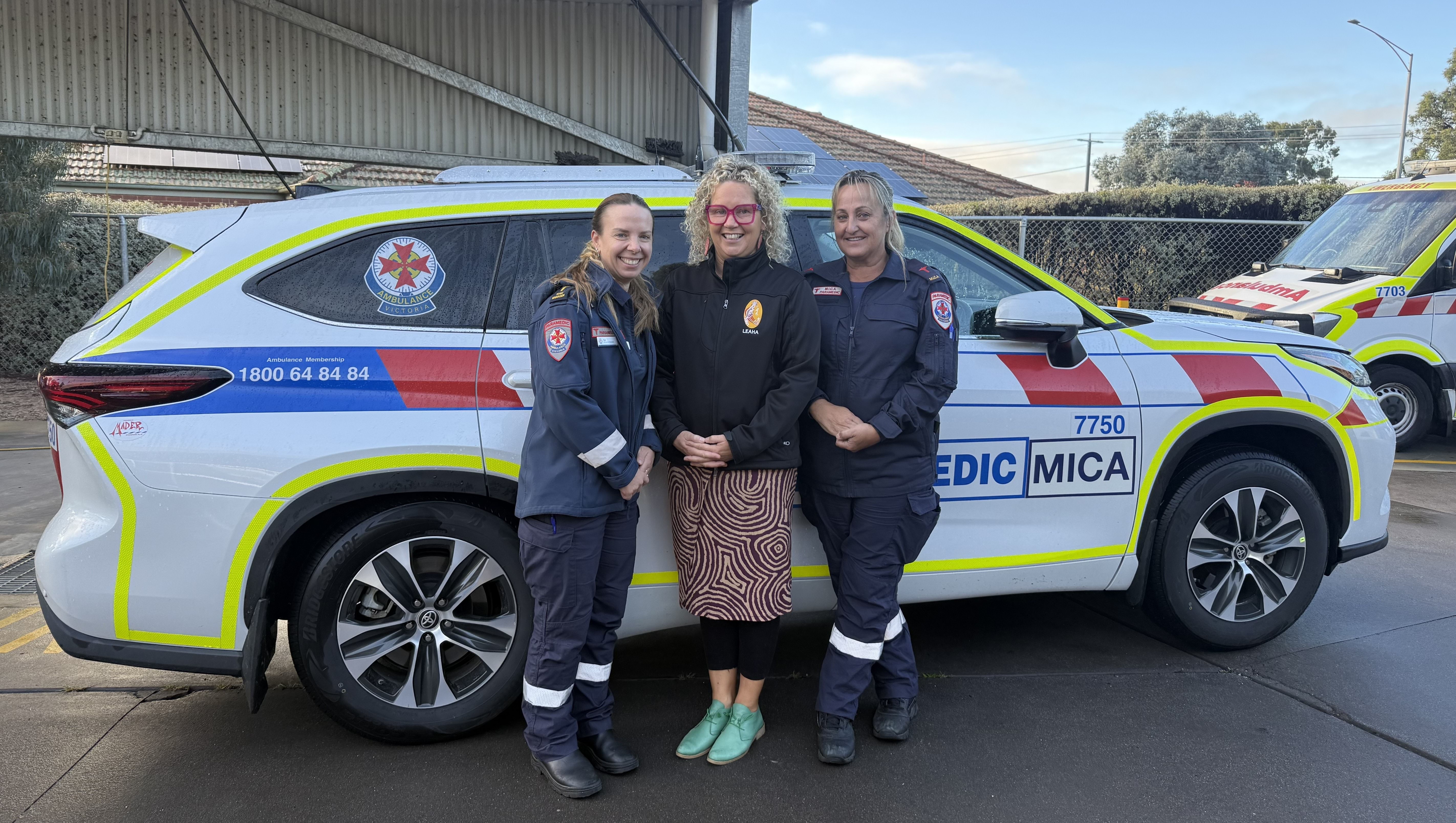 Two paramedics and a woman stand in front of a MICA vehicle.