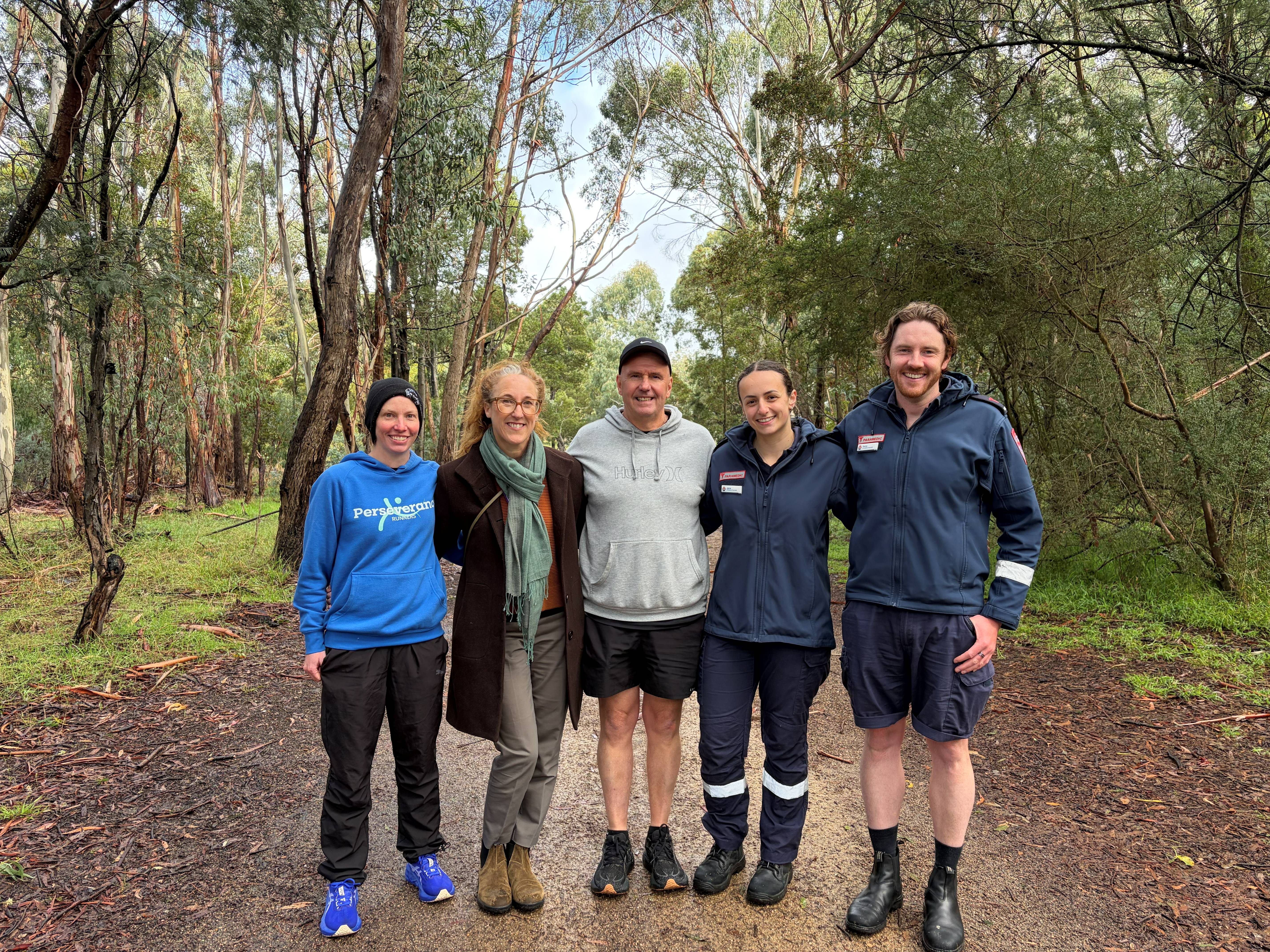 Five people, two in paramedic uniform, smile together on a trail.