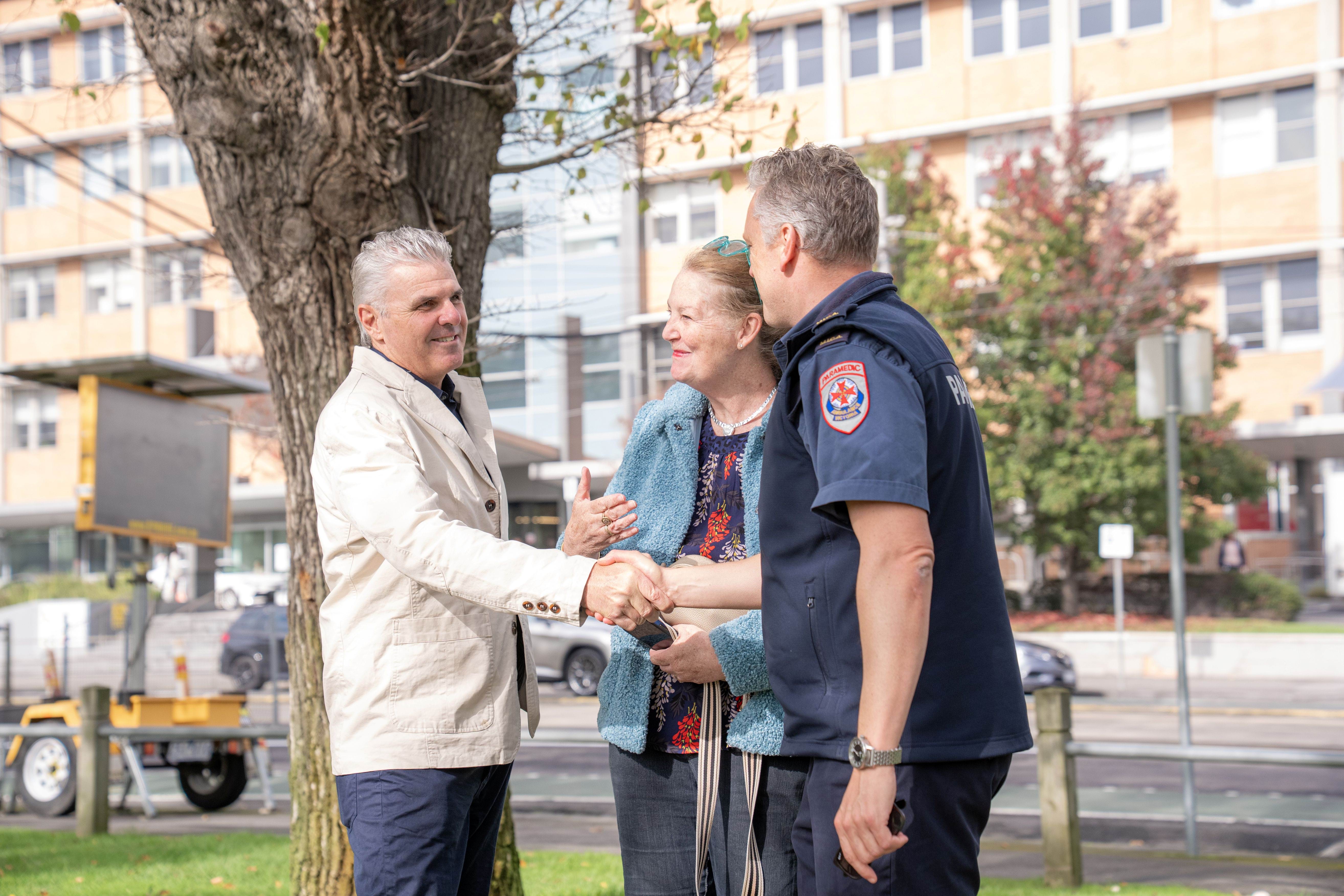 A man shakes hands with a paramedic. A woman smiles.