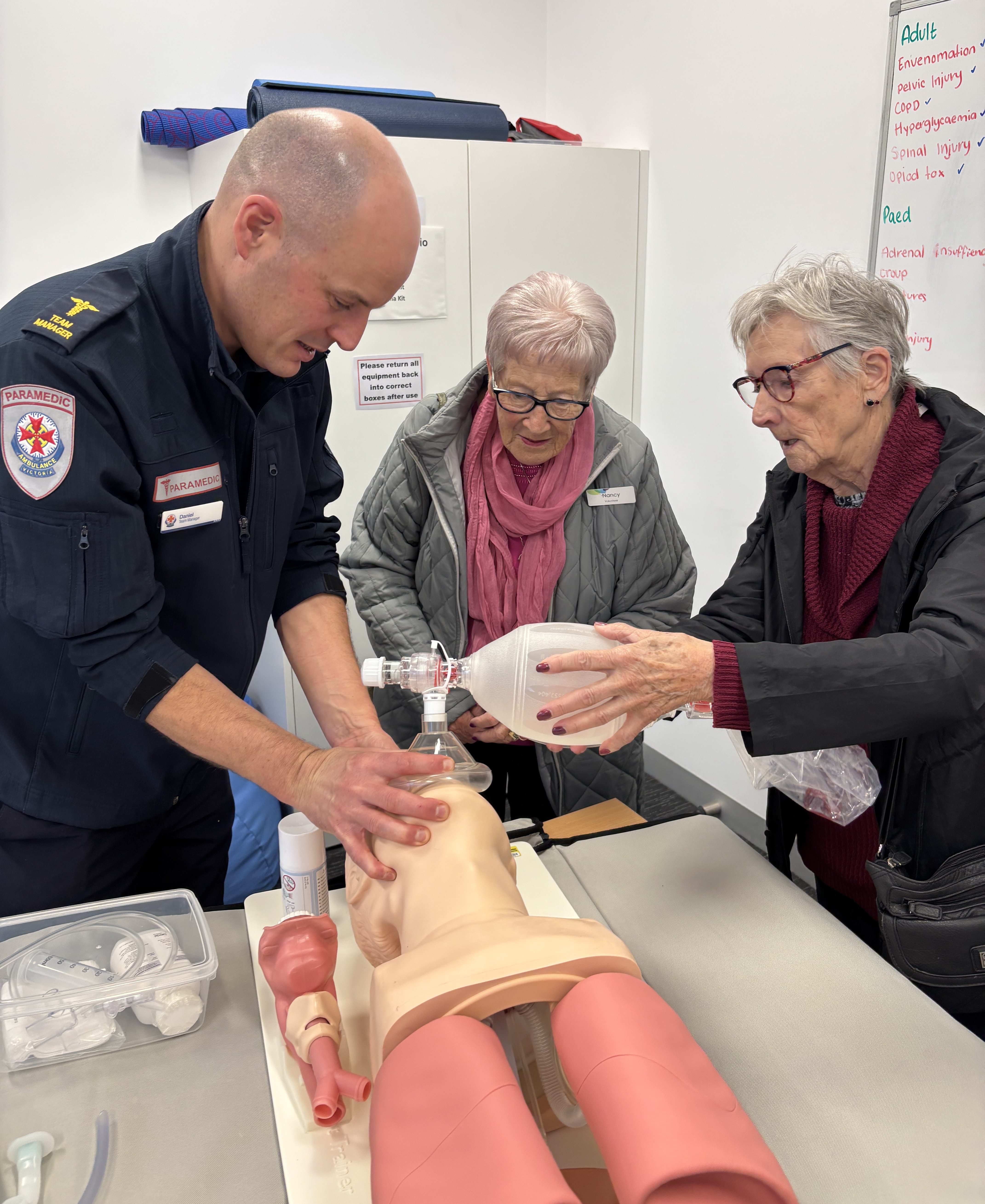 A paramedic showing two ladies how to perform airway management on a manikin.