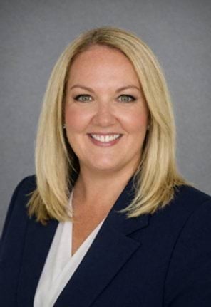 A woman in corporate clothes smiles at the camera in front of a grey background