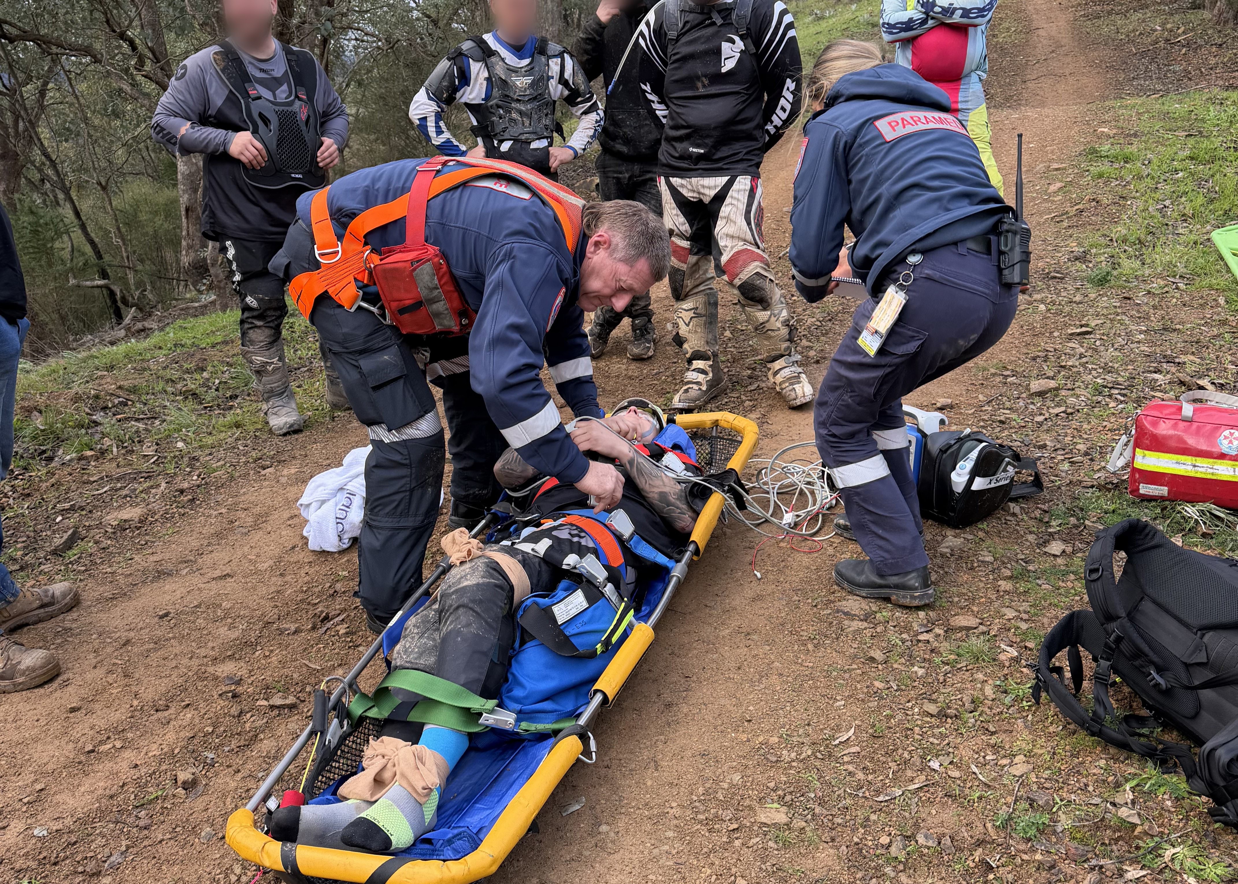 Paramedics treat a patient on a stretcher on a dirt 4WD track.