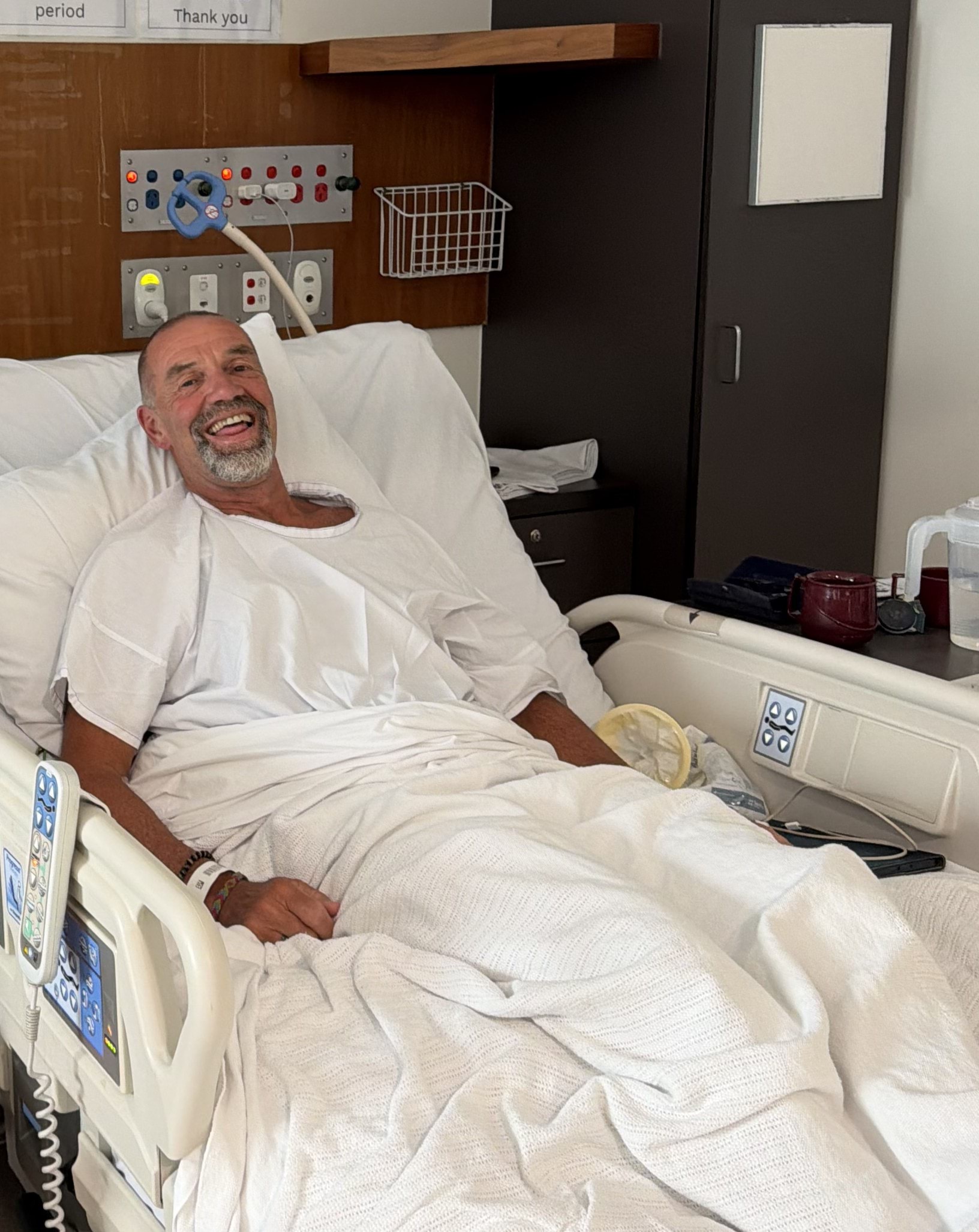 A man smiling while laying in a hospital bed.
