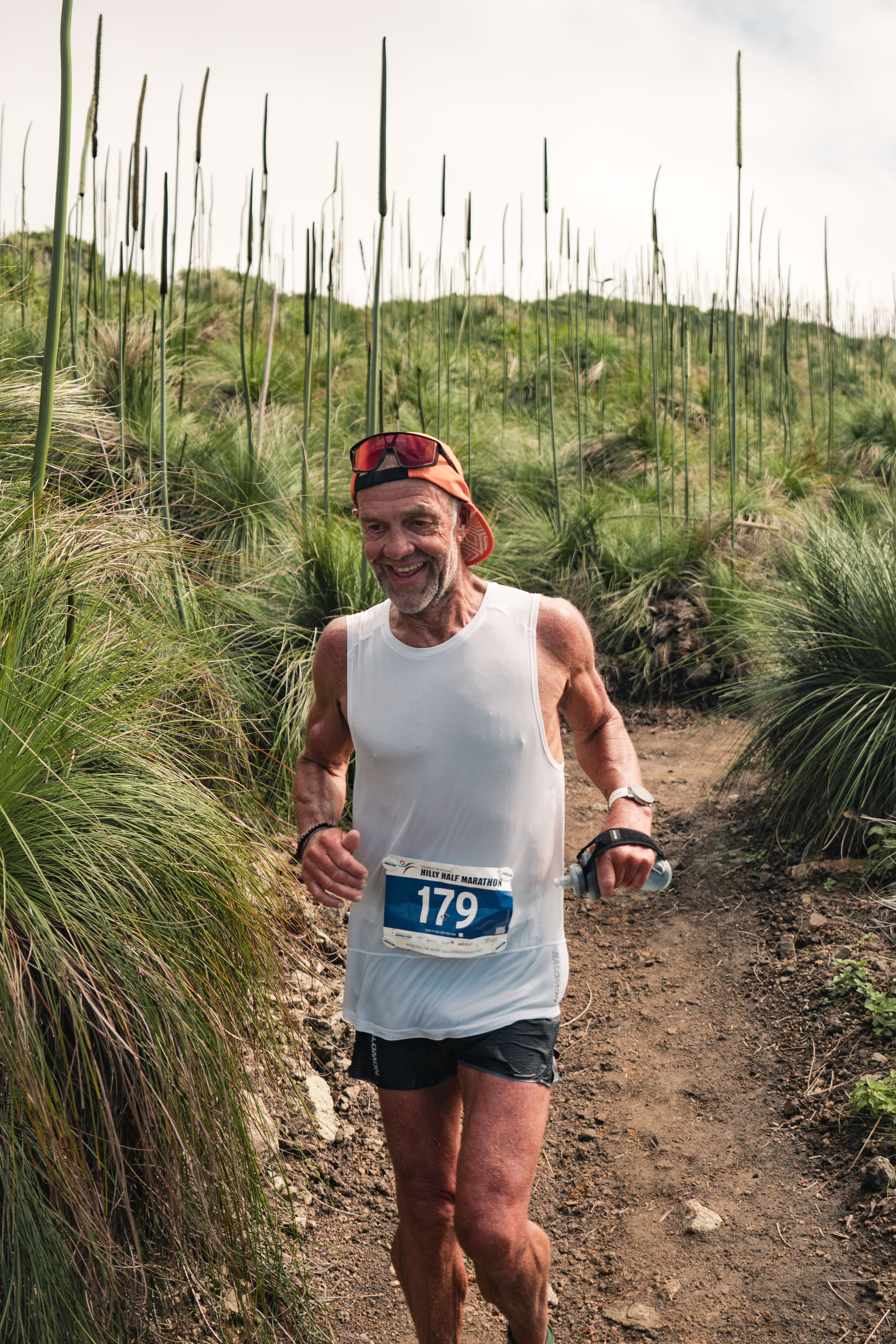 A man running on a trail surrounded by tall grass.