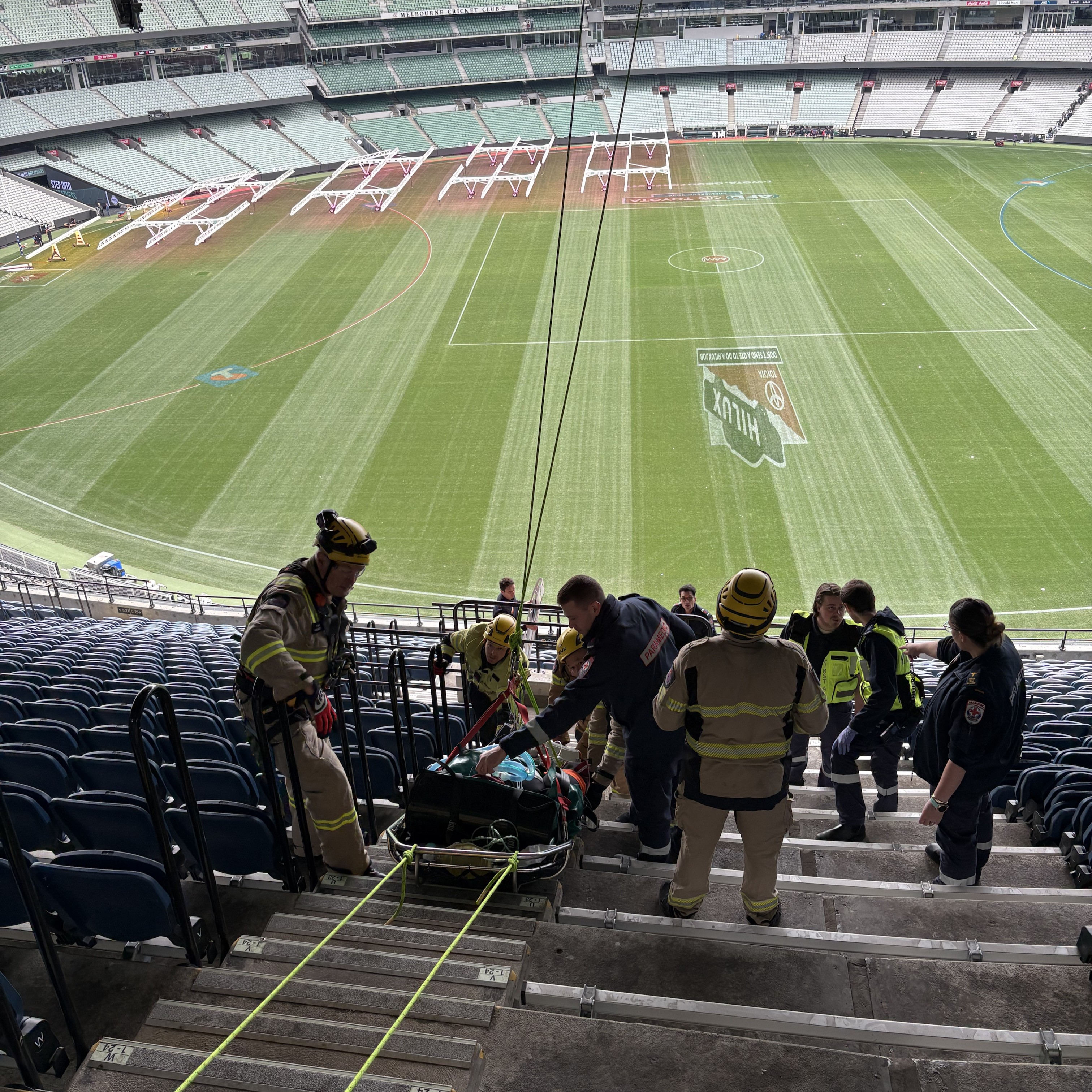 A photo from the top of the MCG stands showing a patient being taken down the stairs on a special stretcher.