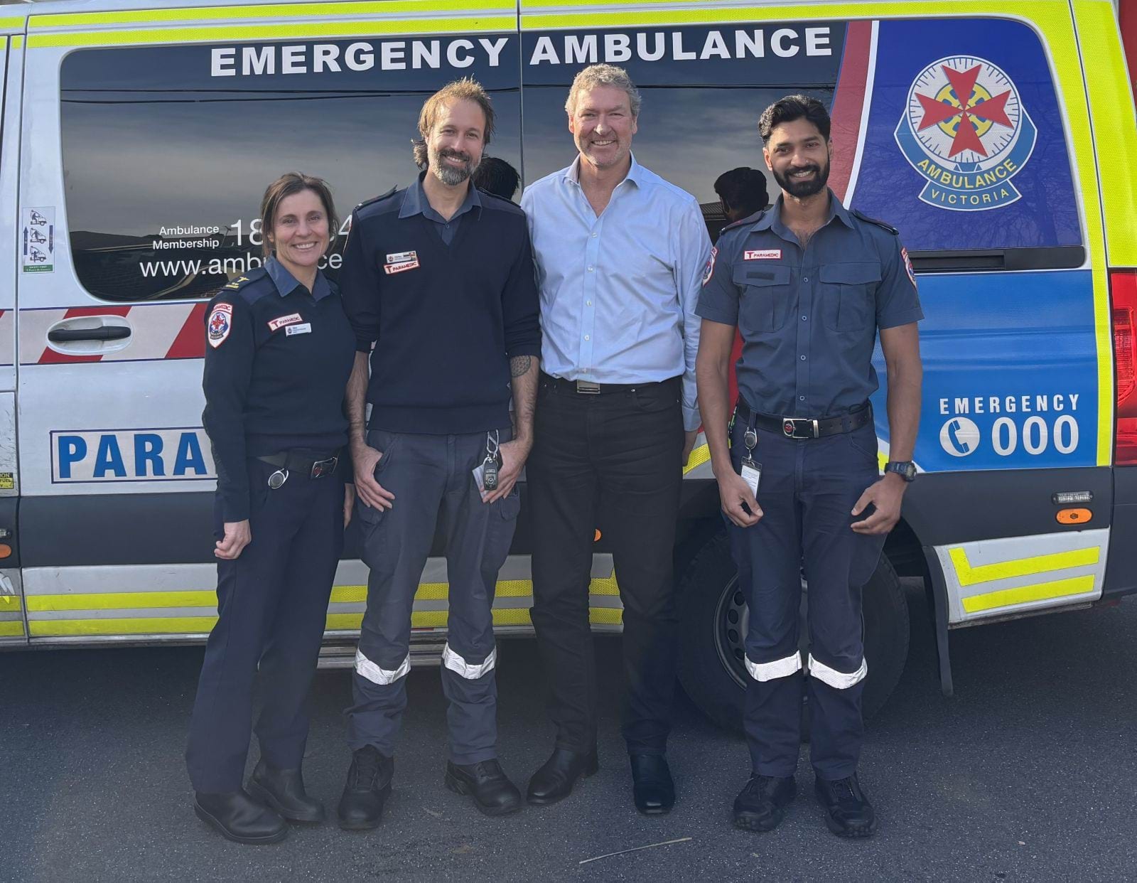 Three paramedics and a man stand in front of an ambulance together