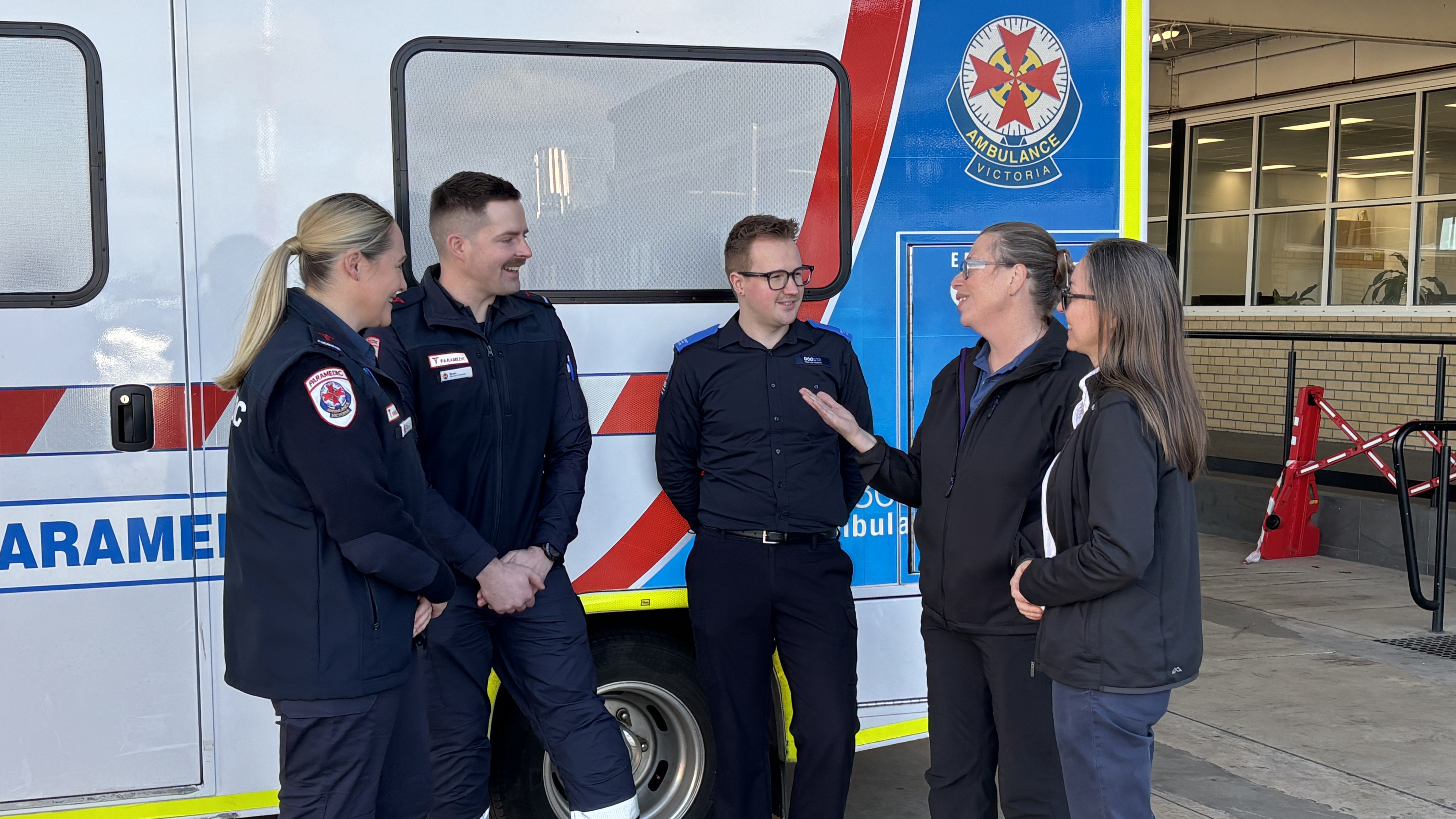 A group of two paramedics, one Triple Zero Victoria call taker and two women chatting in front of an ambulance.