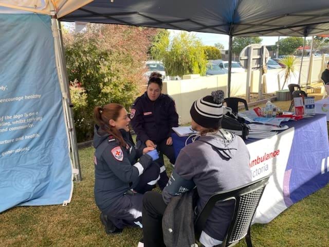 Two paramedics sit outside talking to a patient