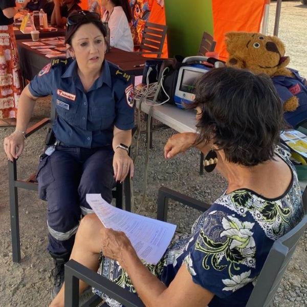 A paramedic sits outside talking to a person in a chair