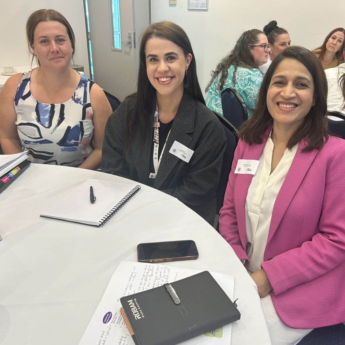 Three women sit at a table at a conference