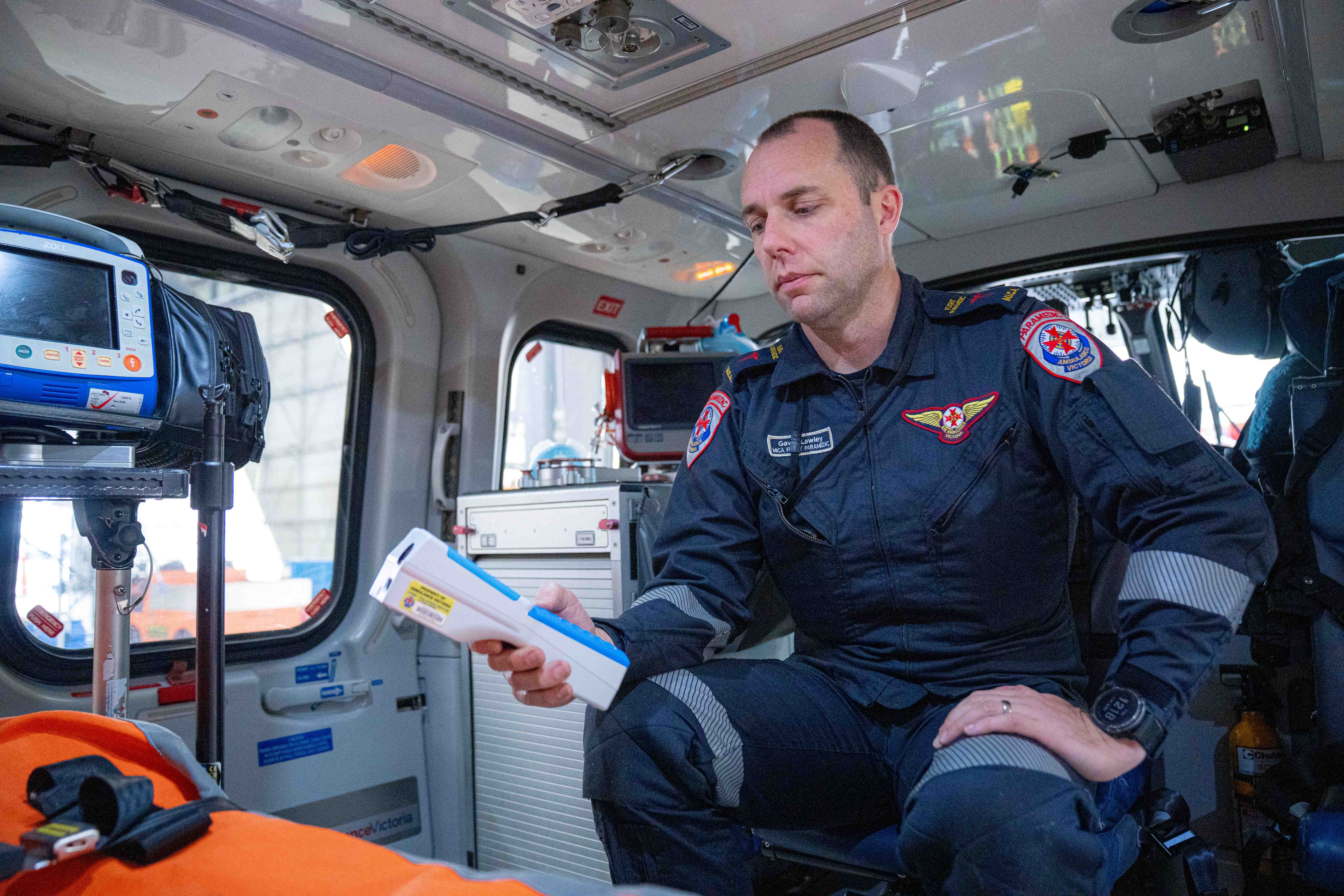 An Ambulance Victoria MICA flight paramedic holds a small medical device inside an air ambulance helicopter.