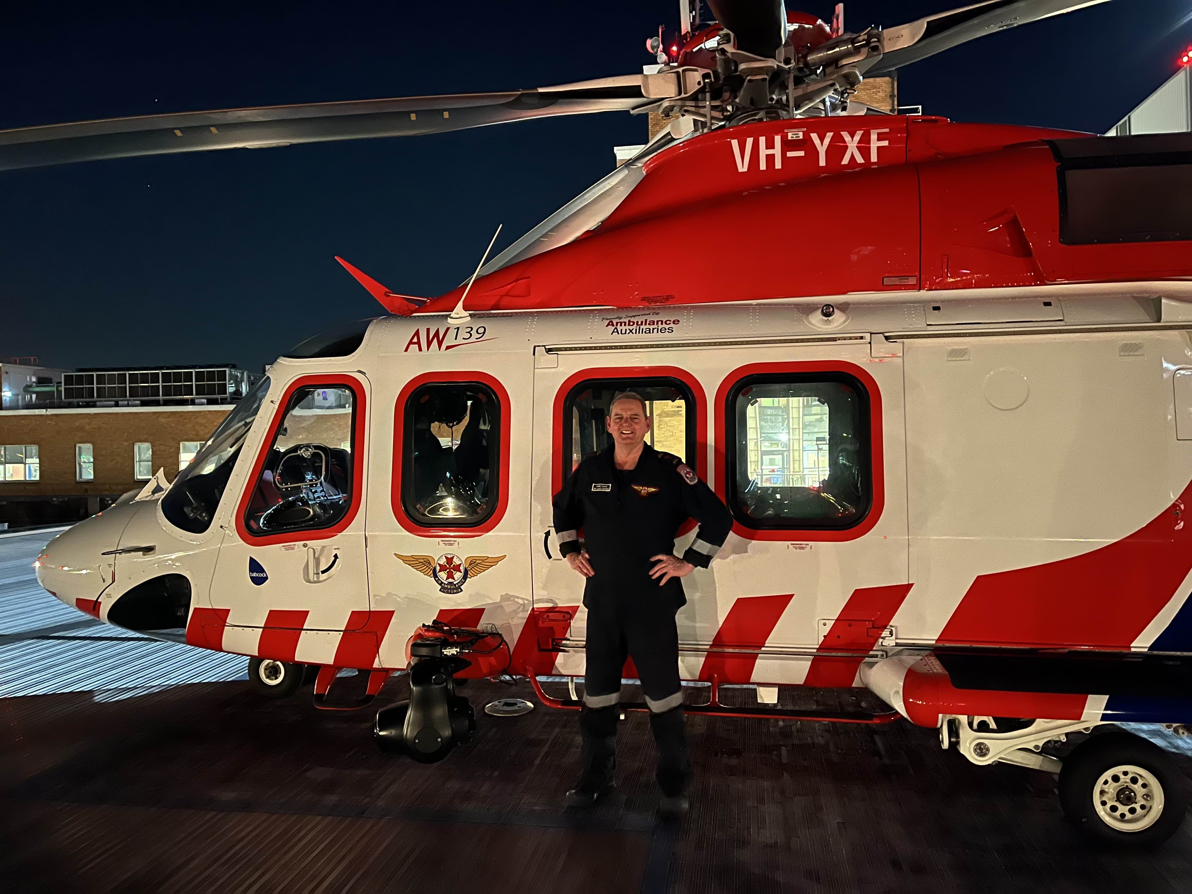 A MICA flight paramedic stands in front of an Ambulance Victoria air ambulance helicopter at night.