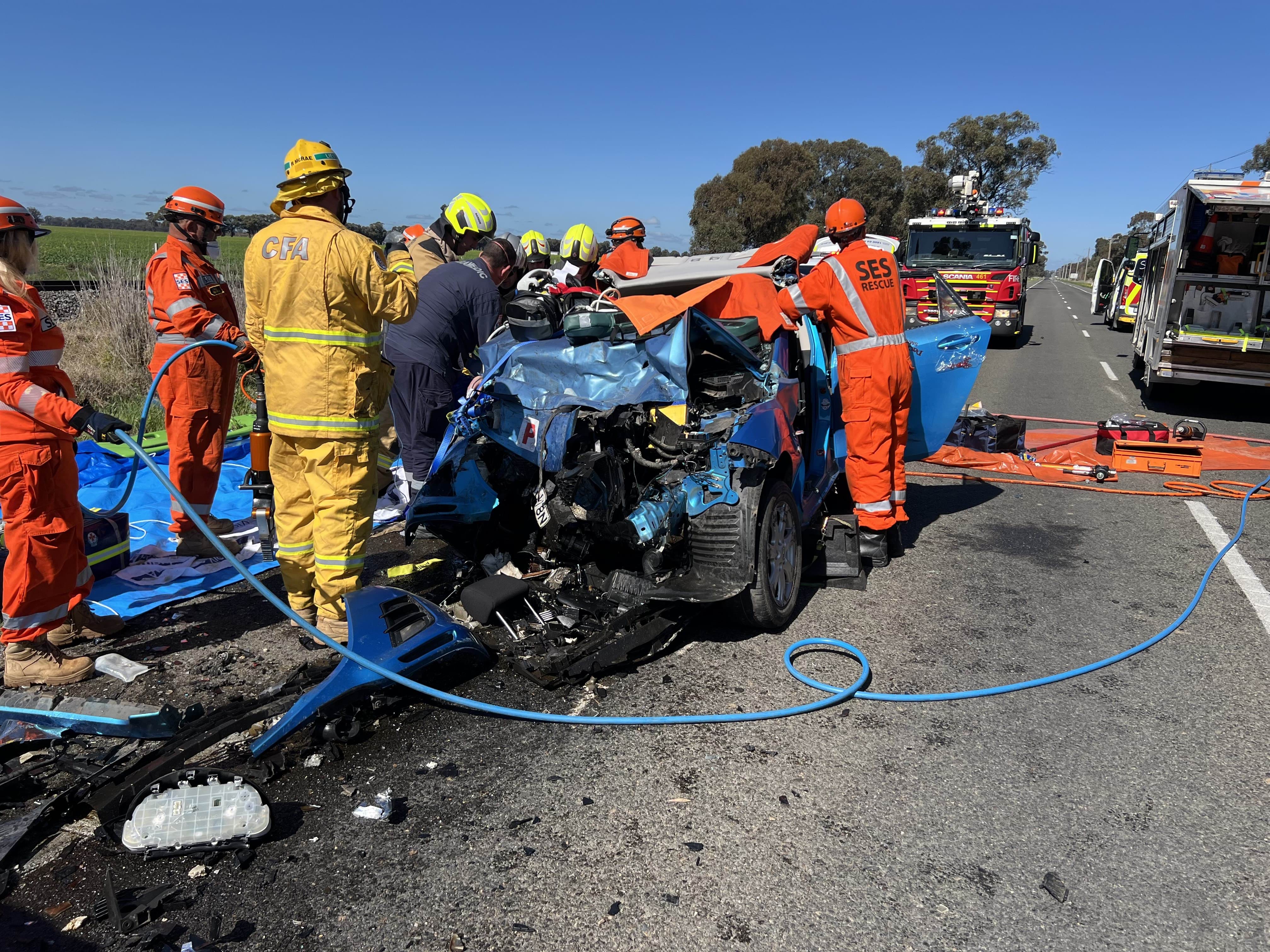 Emergency service workers surround a smashed vehicle on a country road.