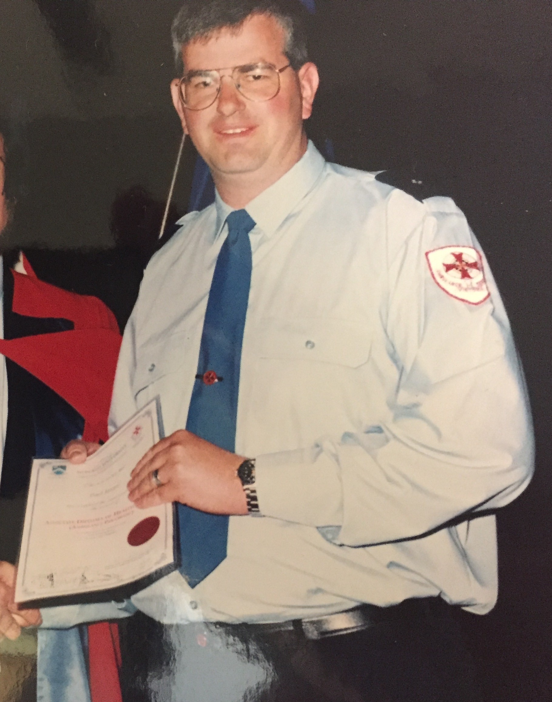 An old colour photo of a man in ambulance dress uniform with a certificate.