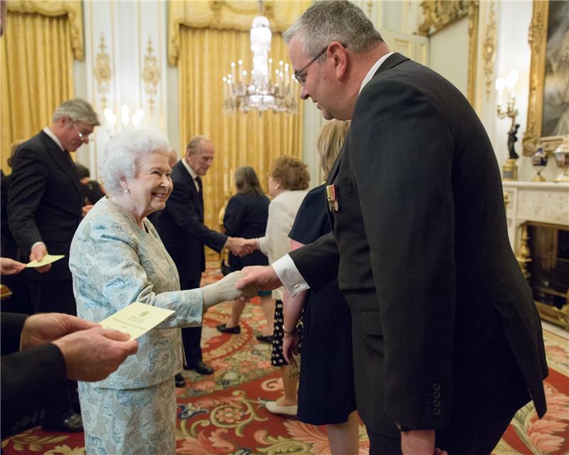 A man in a suit shakes hands with Queen Elizabeth II.