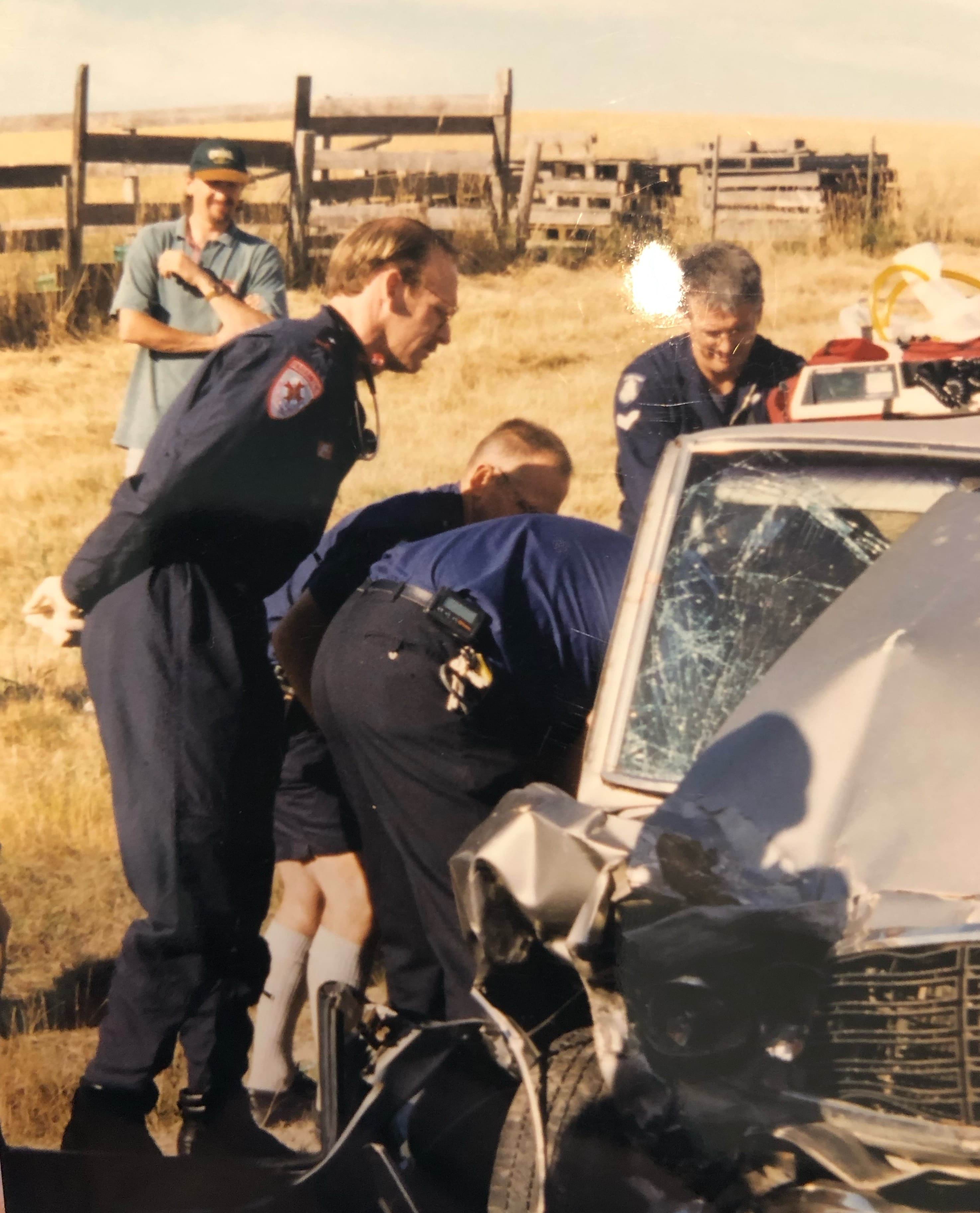 Four male paramedics peering into a vehicle with a crumpled front.
