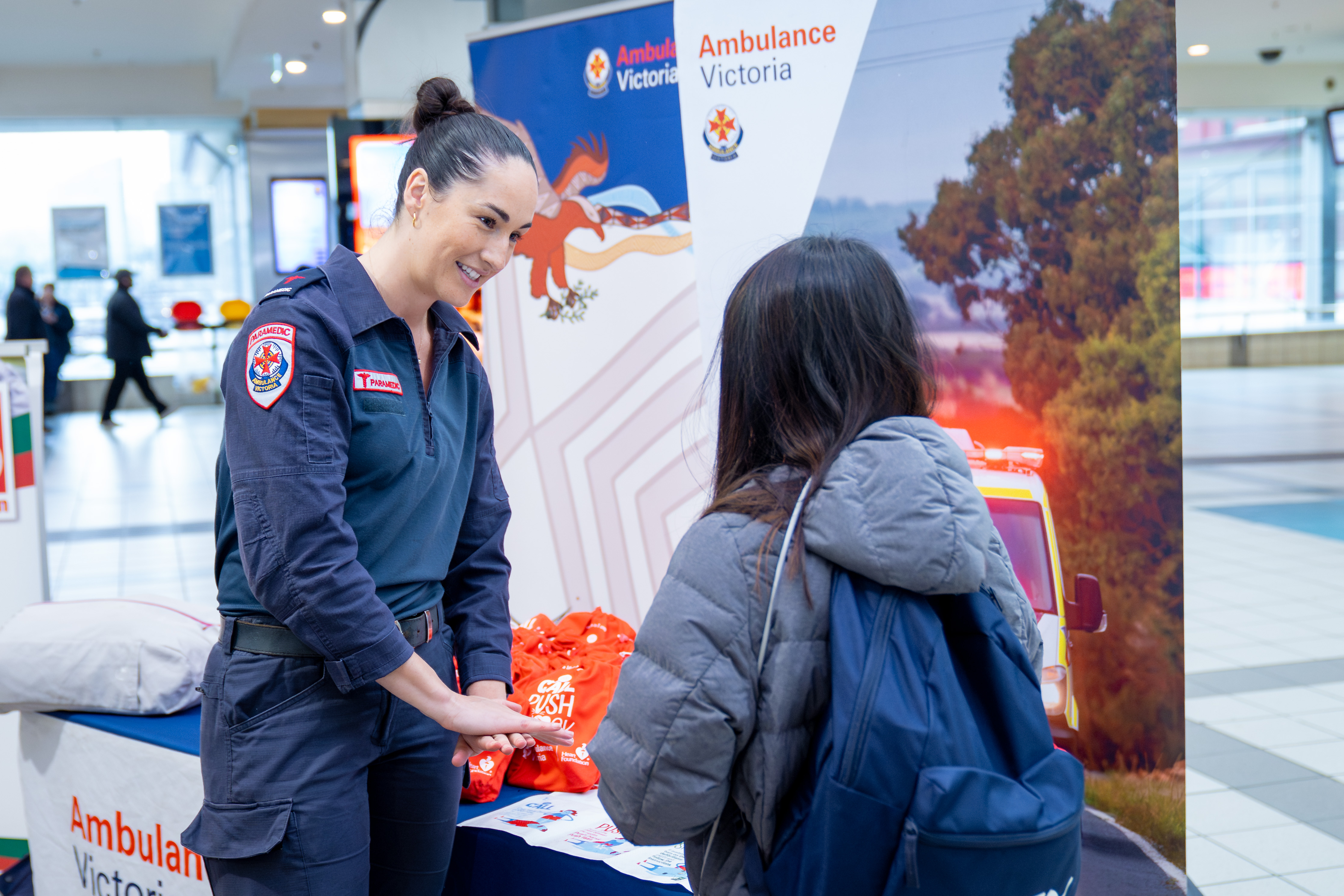 A female paramedic talking to a girl at a counter with standing banners behind it.