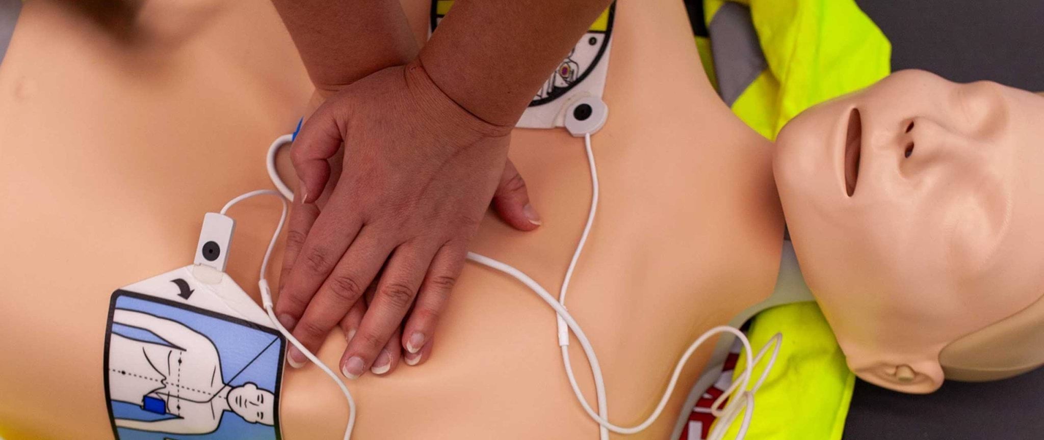 A person practices CPR on a dummy with AED pads attached to the dummy.