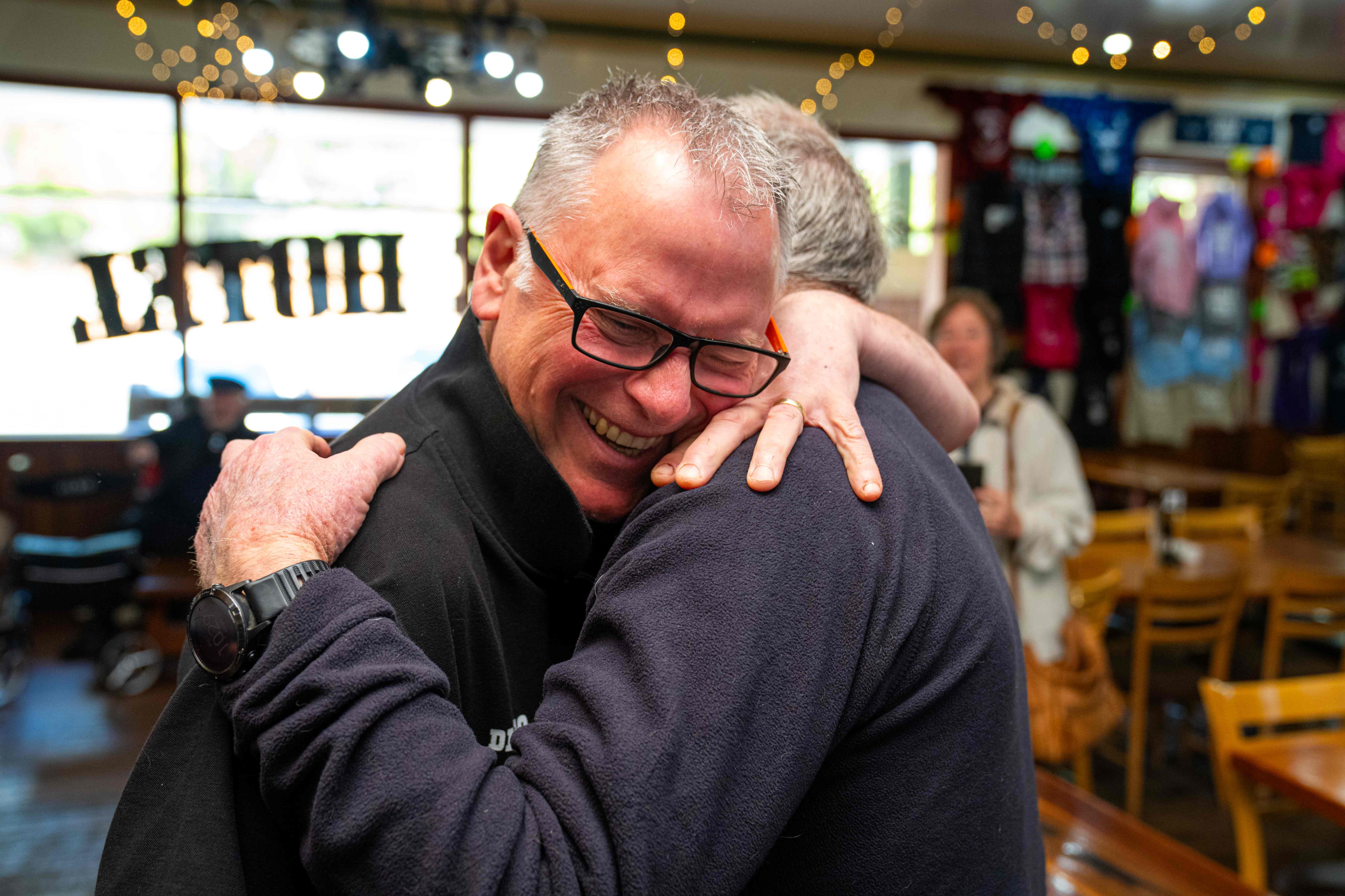 Two men hugging. You can see one man smiling while resting his head on the shoulder of the man he's hugging.