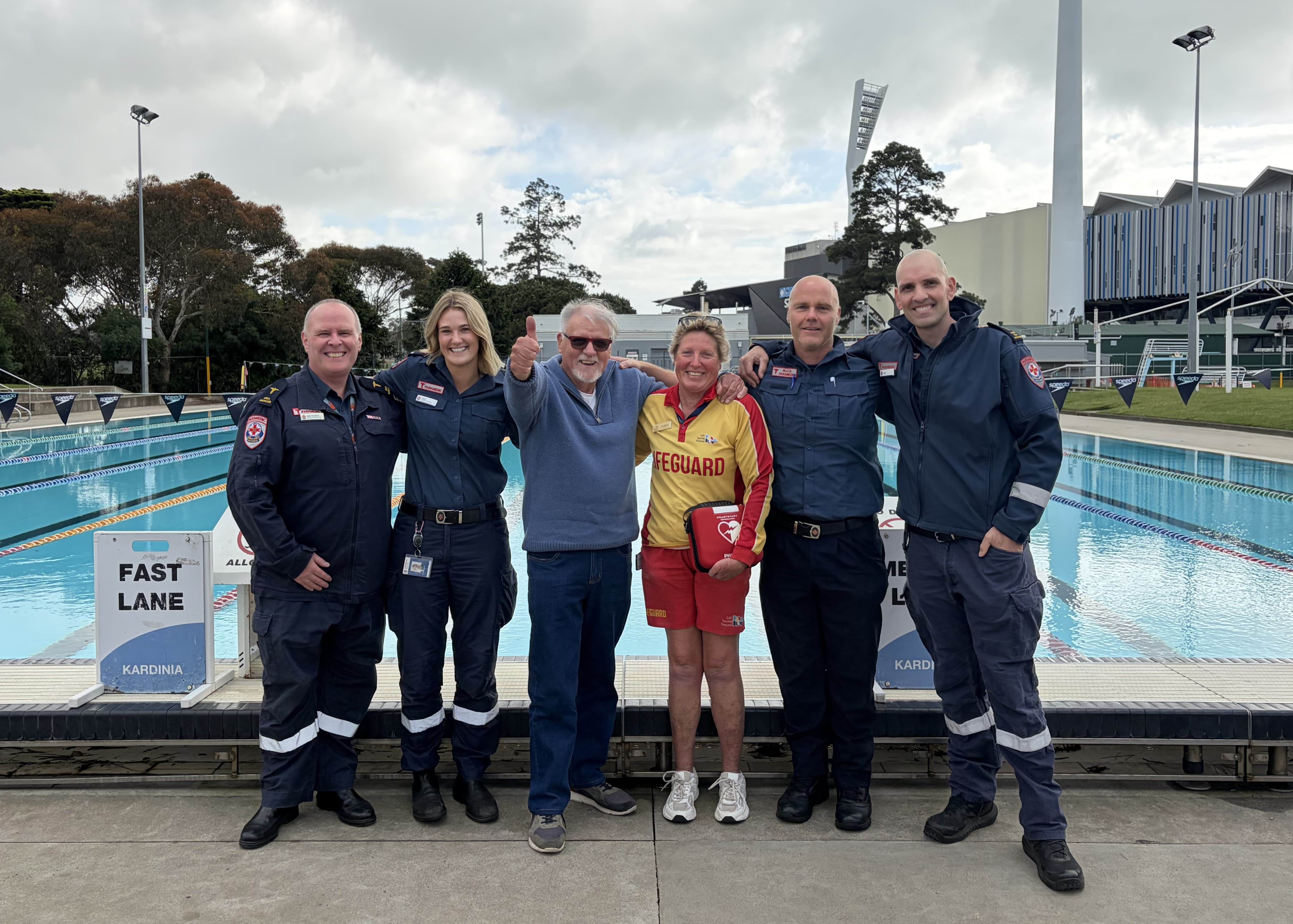 A man in casual clothes gives a thumbs up next to a lifeguard and four paramedics.