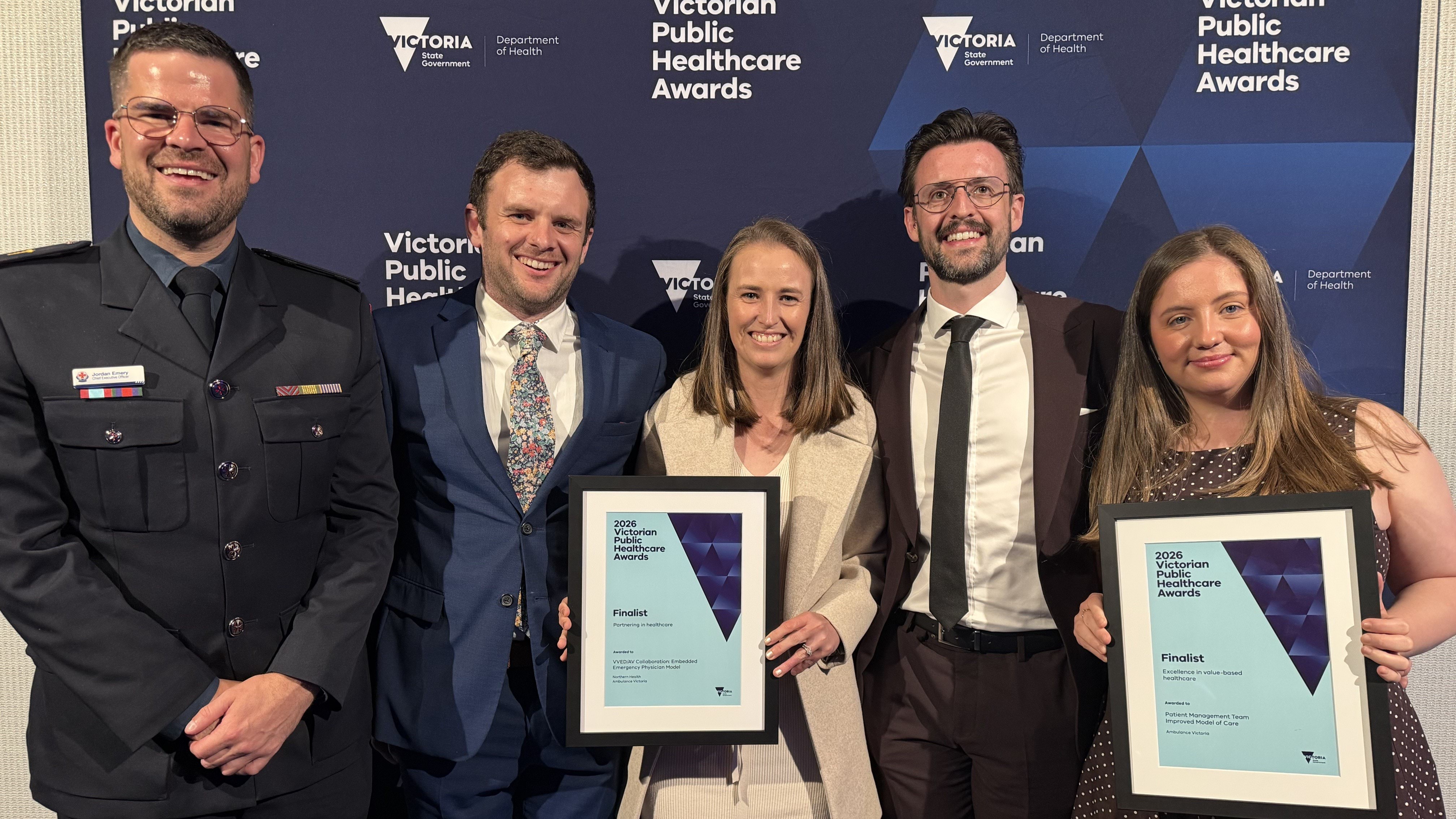 A group of five smiling people. Two of the people are holding framed certificates. 
