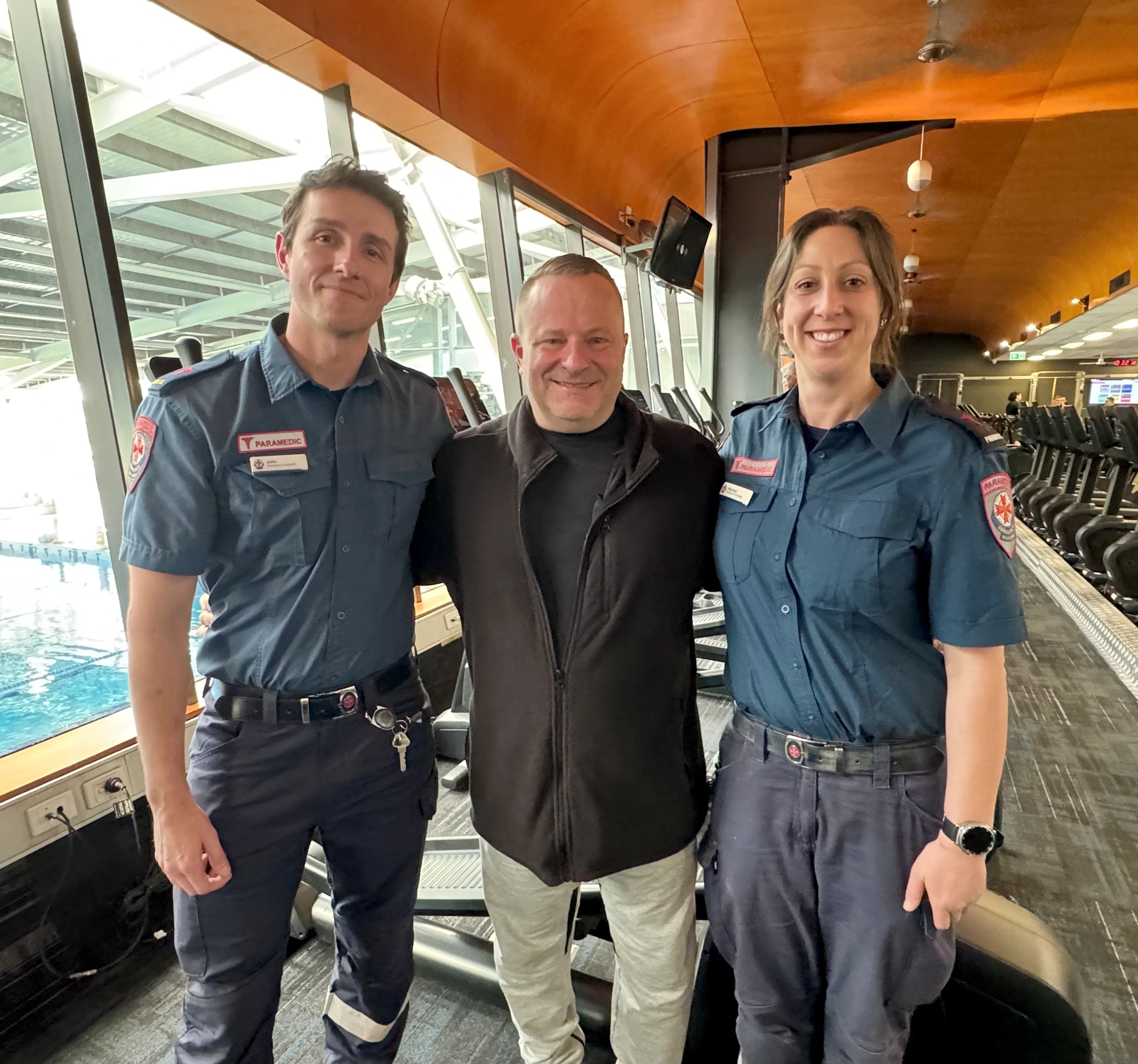Two Ambulance Victoria paramedics dressed in blue uniform with patient Adam Heitmann dressed in black in between them