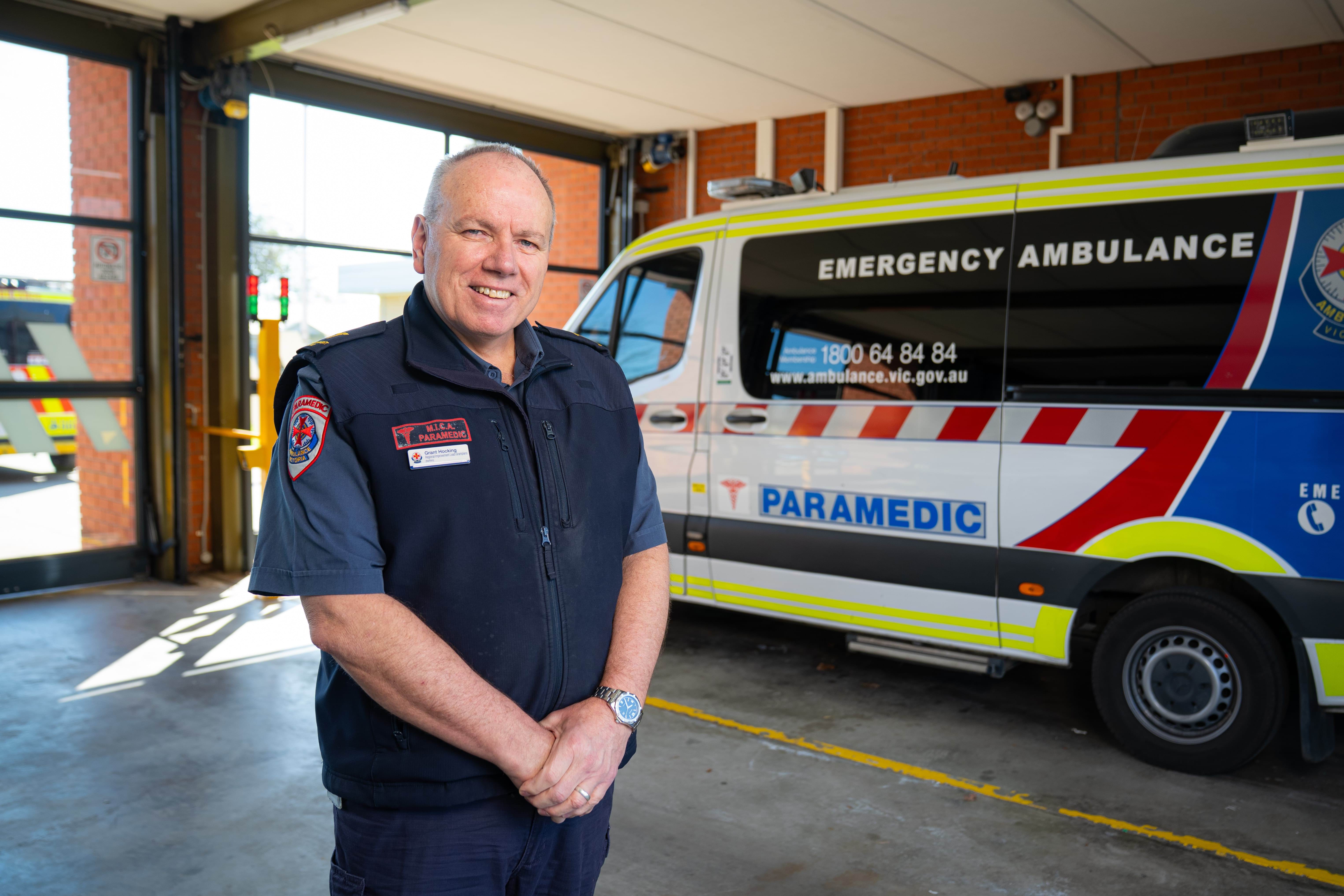 A MICA paramedic smiles in front of an ambulance vehicle.
