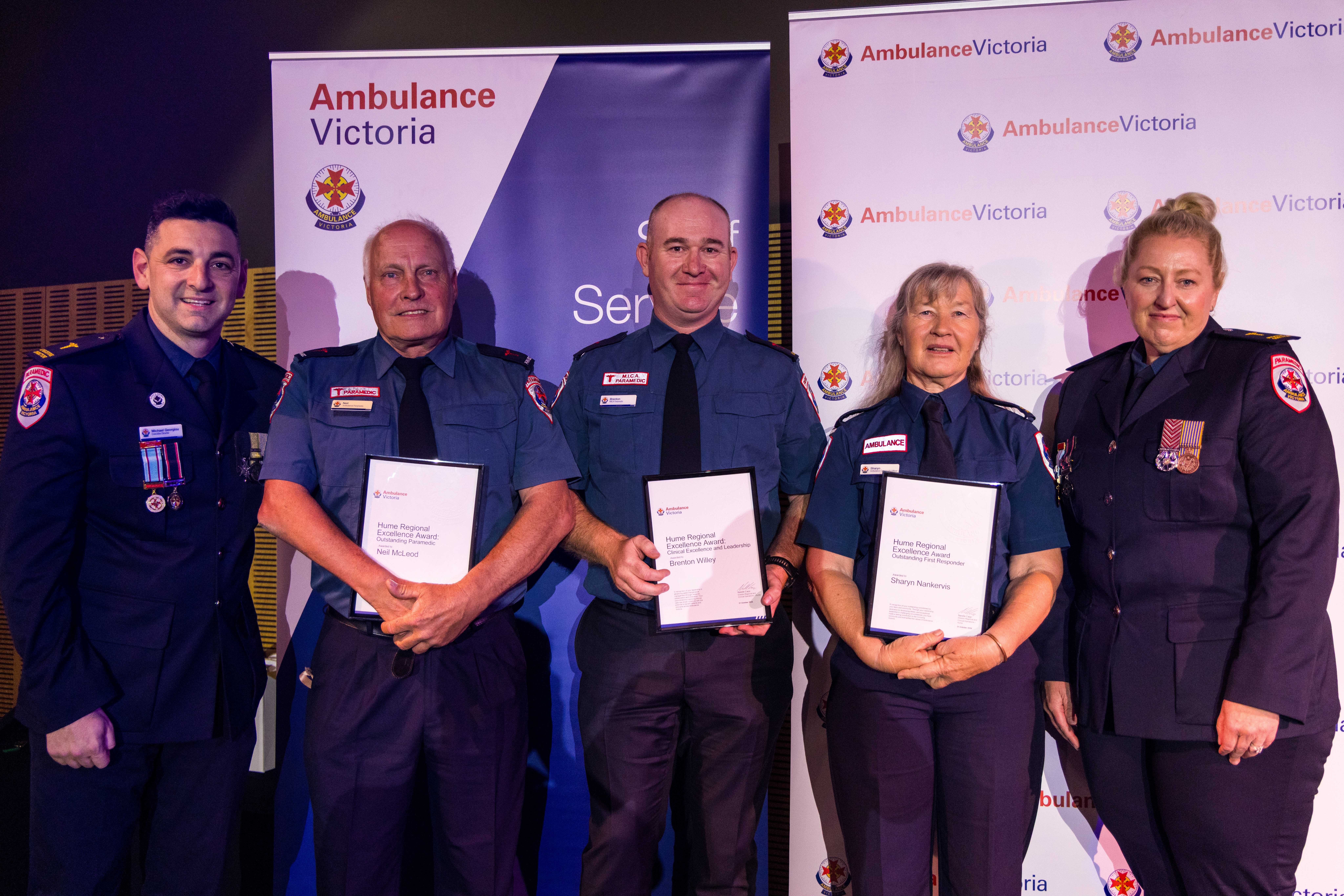 Five people in Ambulance Victoria dress uniform smile for the camera. The middle three people hold certificates.
