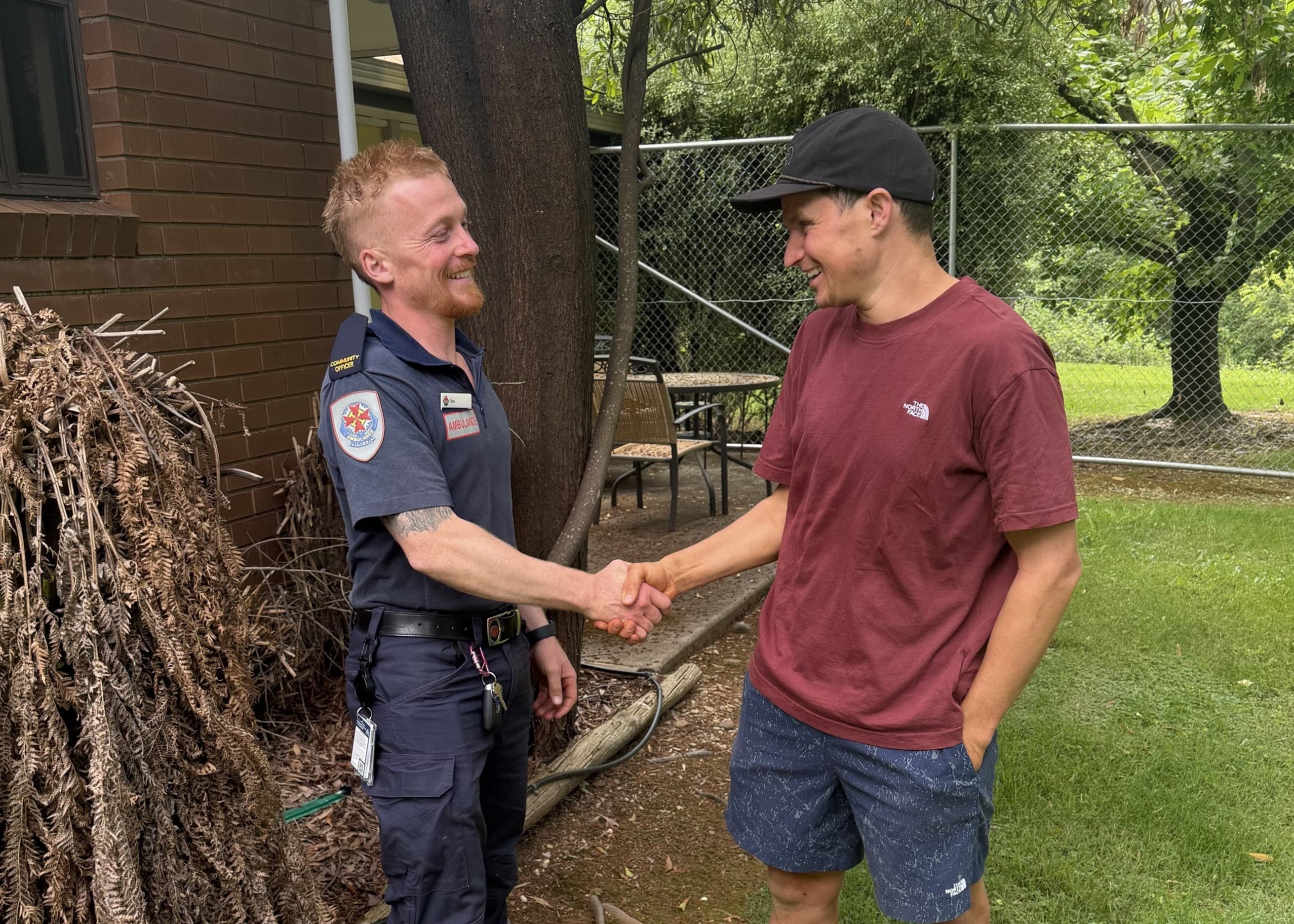 A man shakes hands with another man in Ambulance Victoria uniform.
