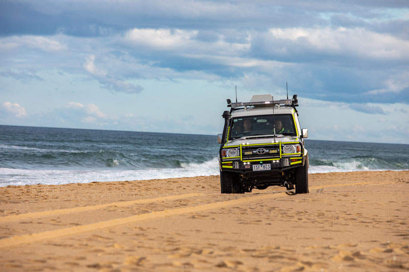 A four wheel drive ambulance drives along the sand on a beach