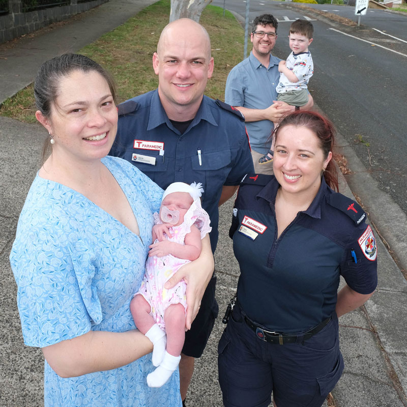 A mother stands with two paramedics and a man and child beside a road